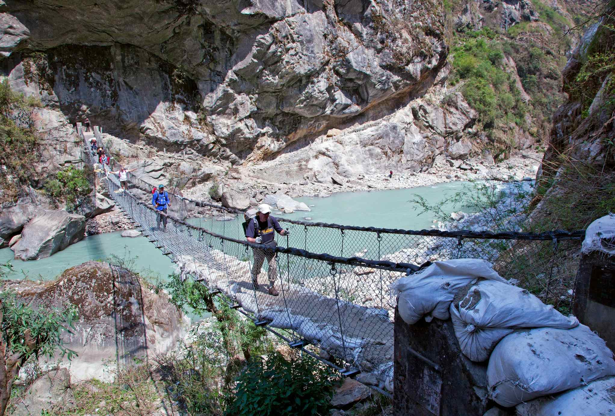 Two hikers crossing a Himalayan rope bridge above a river, Nepal