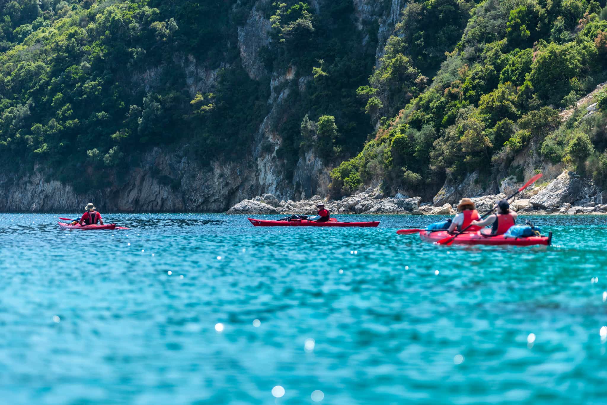 Kayakers by the rocky shoreline of the Ionian Islands in Greece.