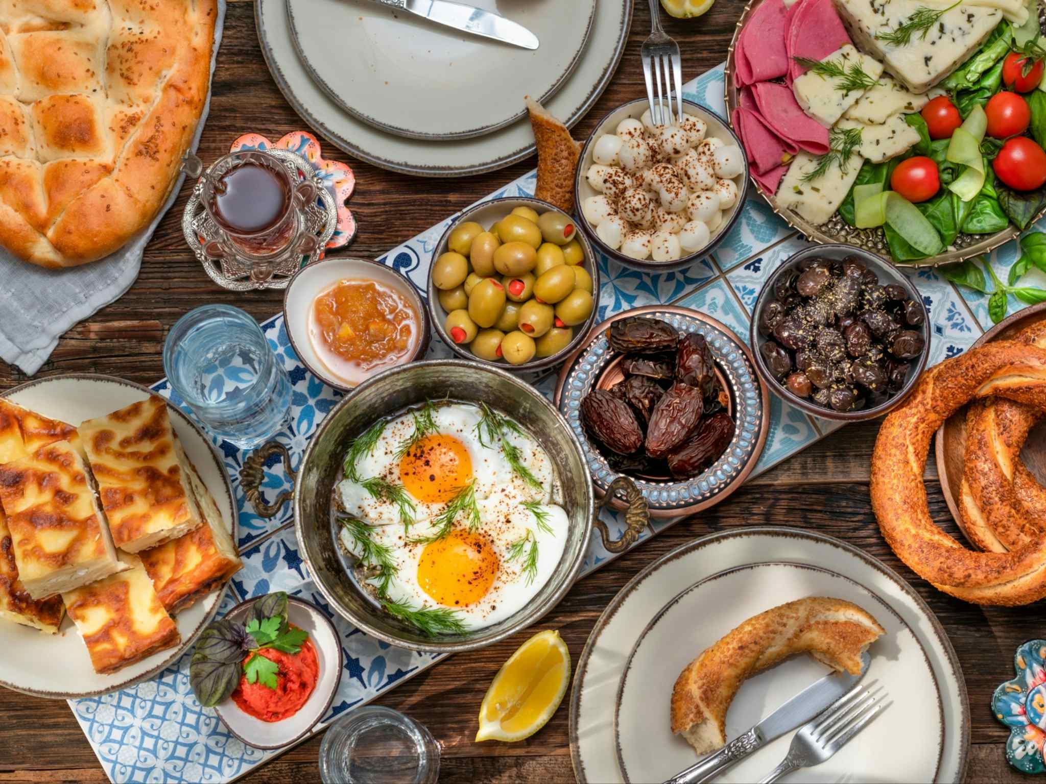 Traditional Turkish breakfast include tomatoes, cucumbers, cheese, butter, eggs, honey, bread, bagels, olives and tea cups. shutterstock 1940339386