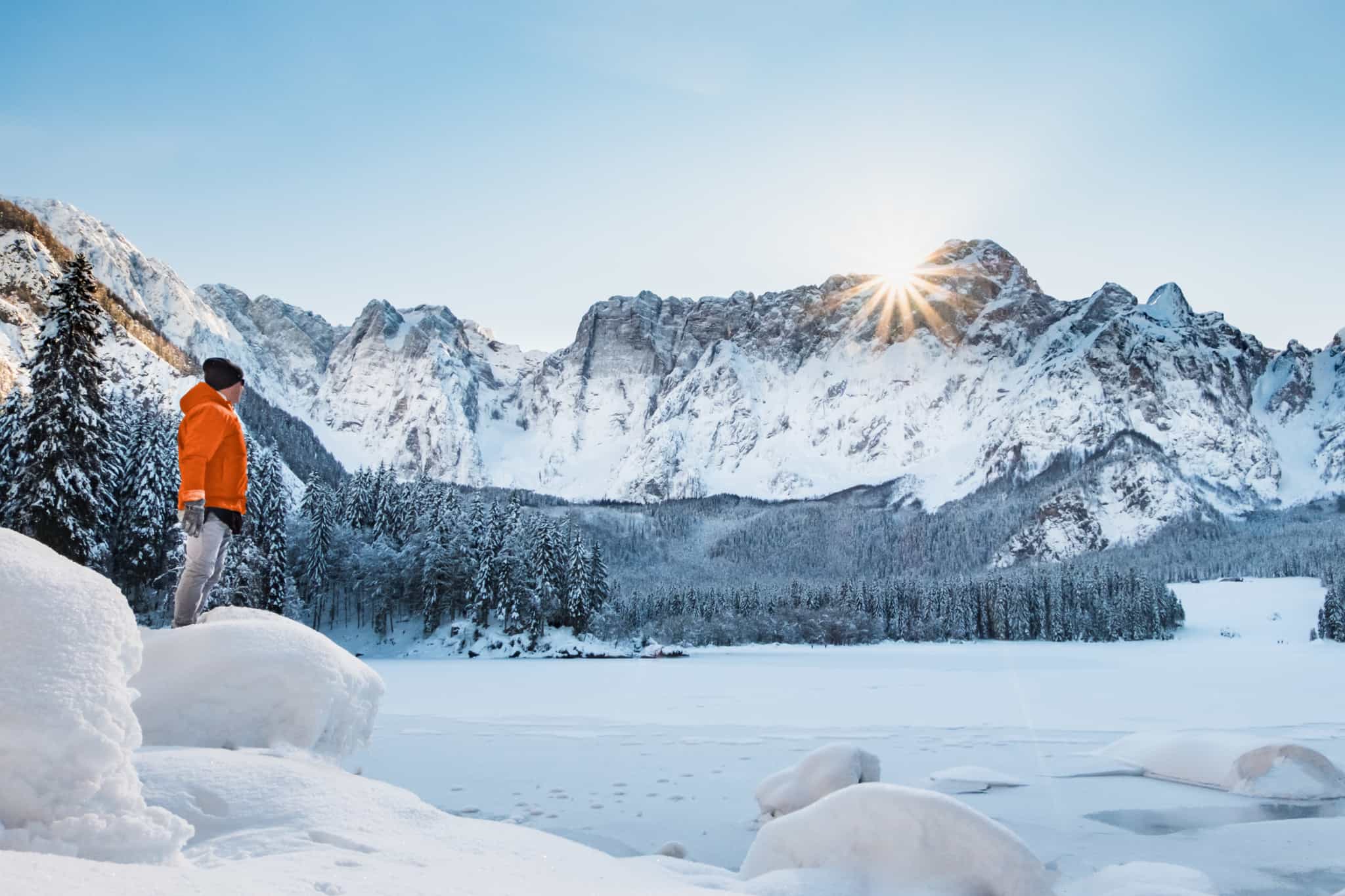 Hiker looking out acrossFusine Lake in the snow, Italy