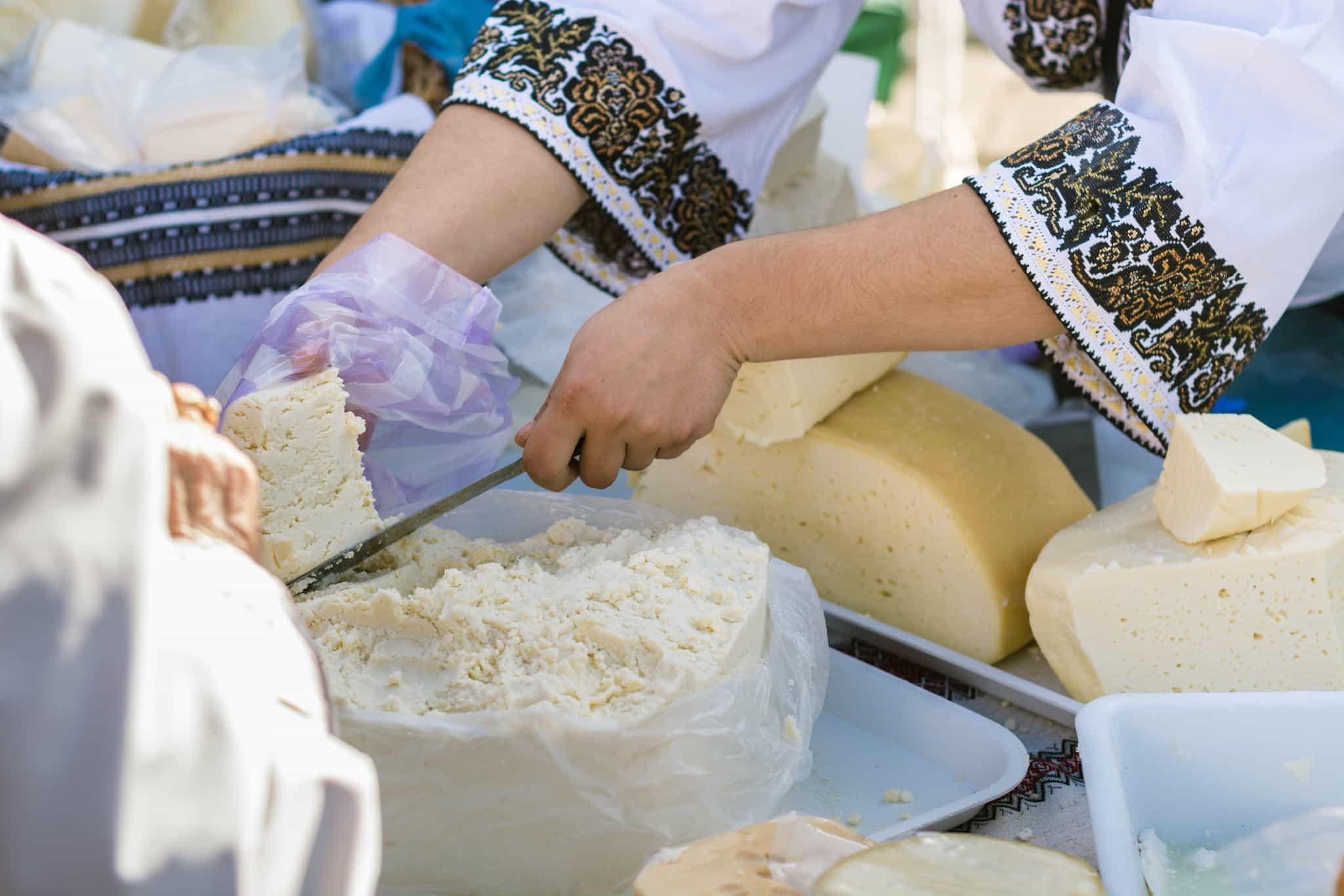 Women hands cutting traditional Romanian cheese on a table in a market.