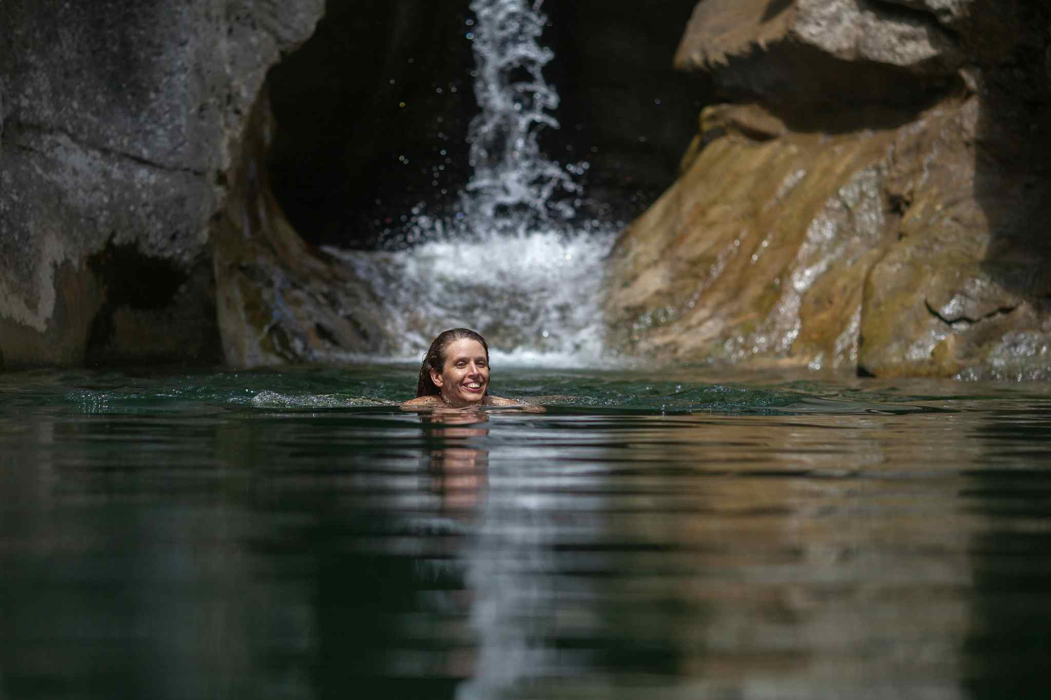 Woman swimming in a natural pool backed by a waterfall and rocks, Costa Rica.