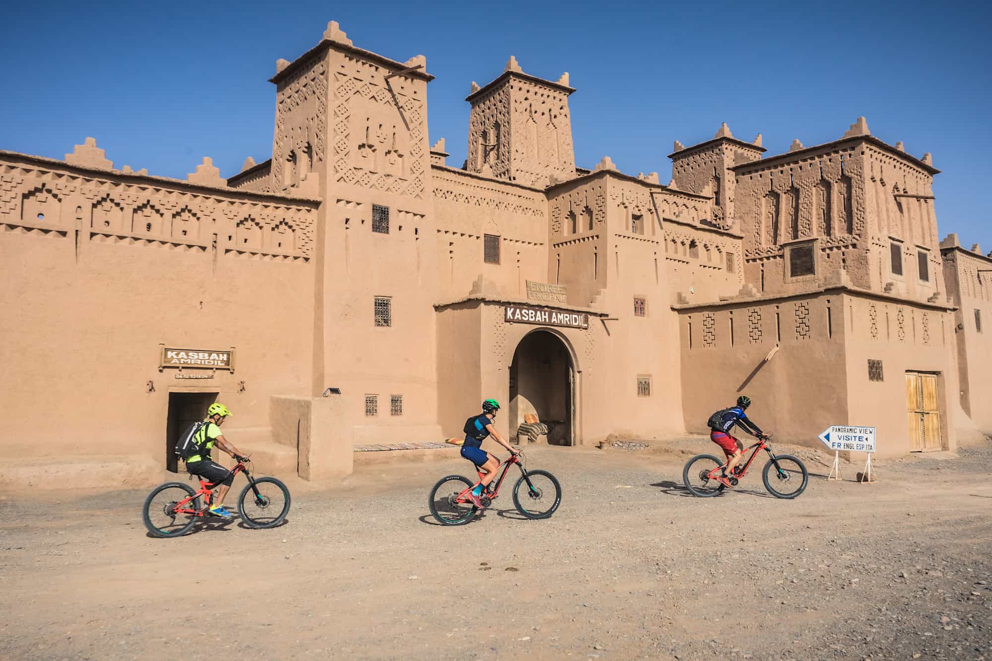Three cyclists riding past Ait Ben Haddou, Morocco