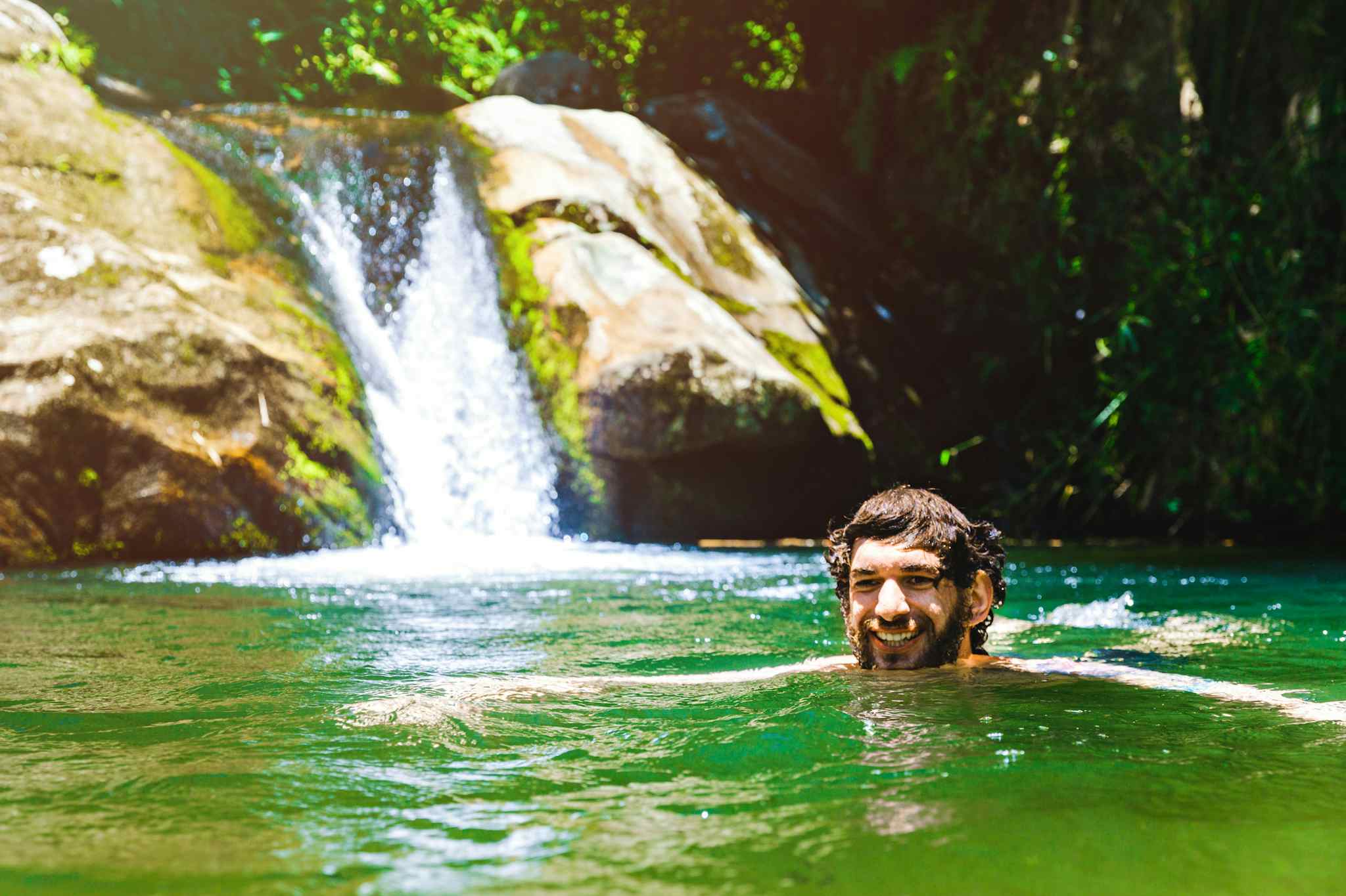 Man swimming in a pool backed by a waterfall, Costa Rica.