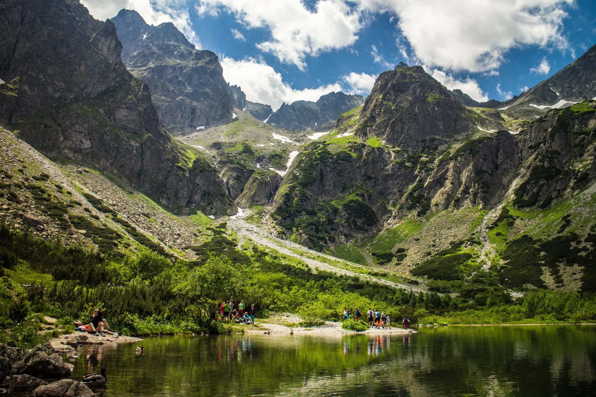 Hiking group relaxing at a mountain lake below high the high peaks of the Tatras