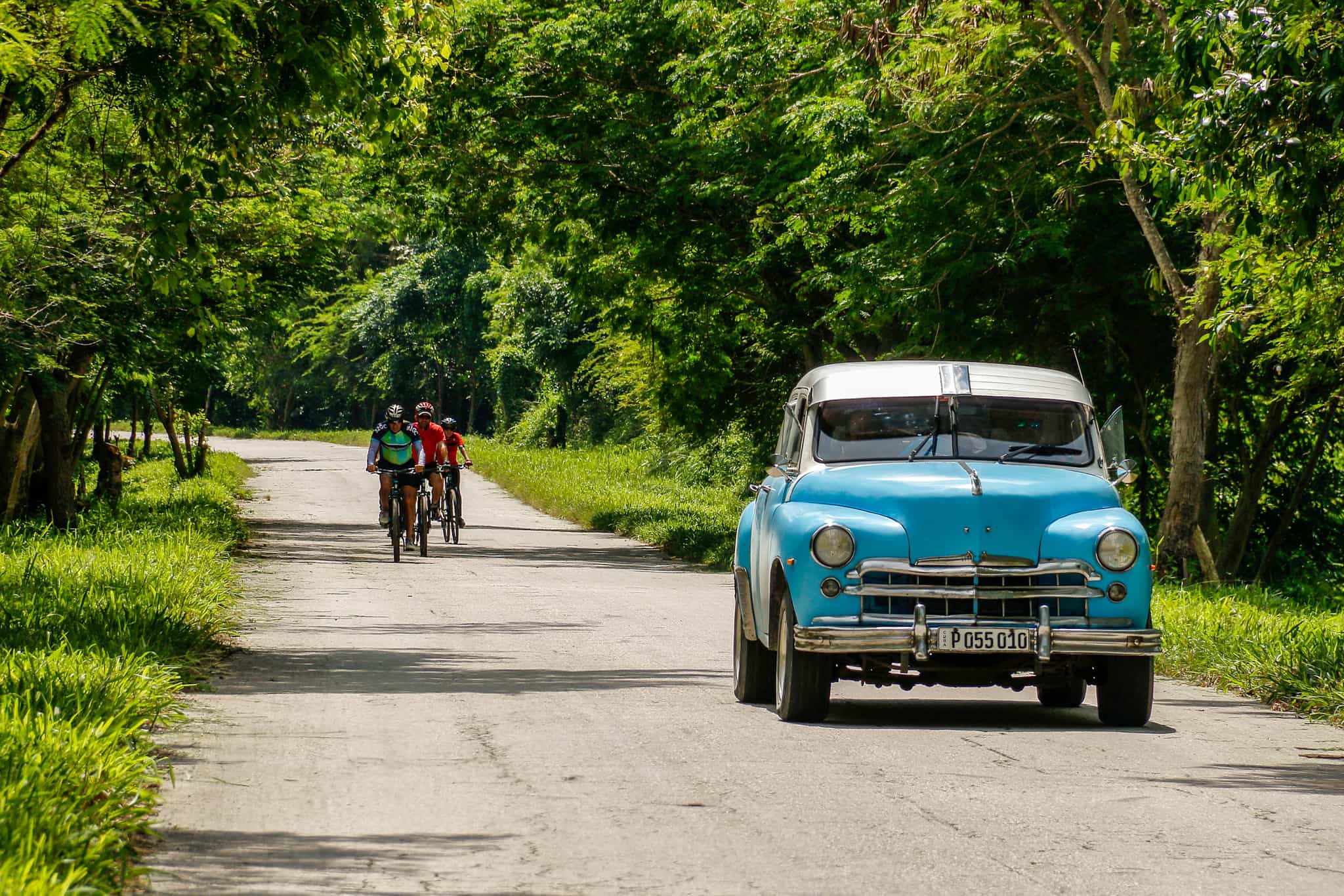 Cycling past blue classic car in Cuba