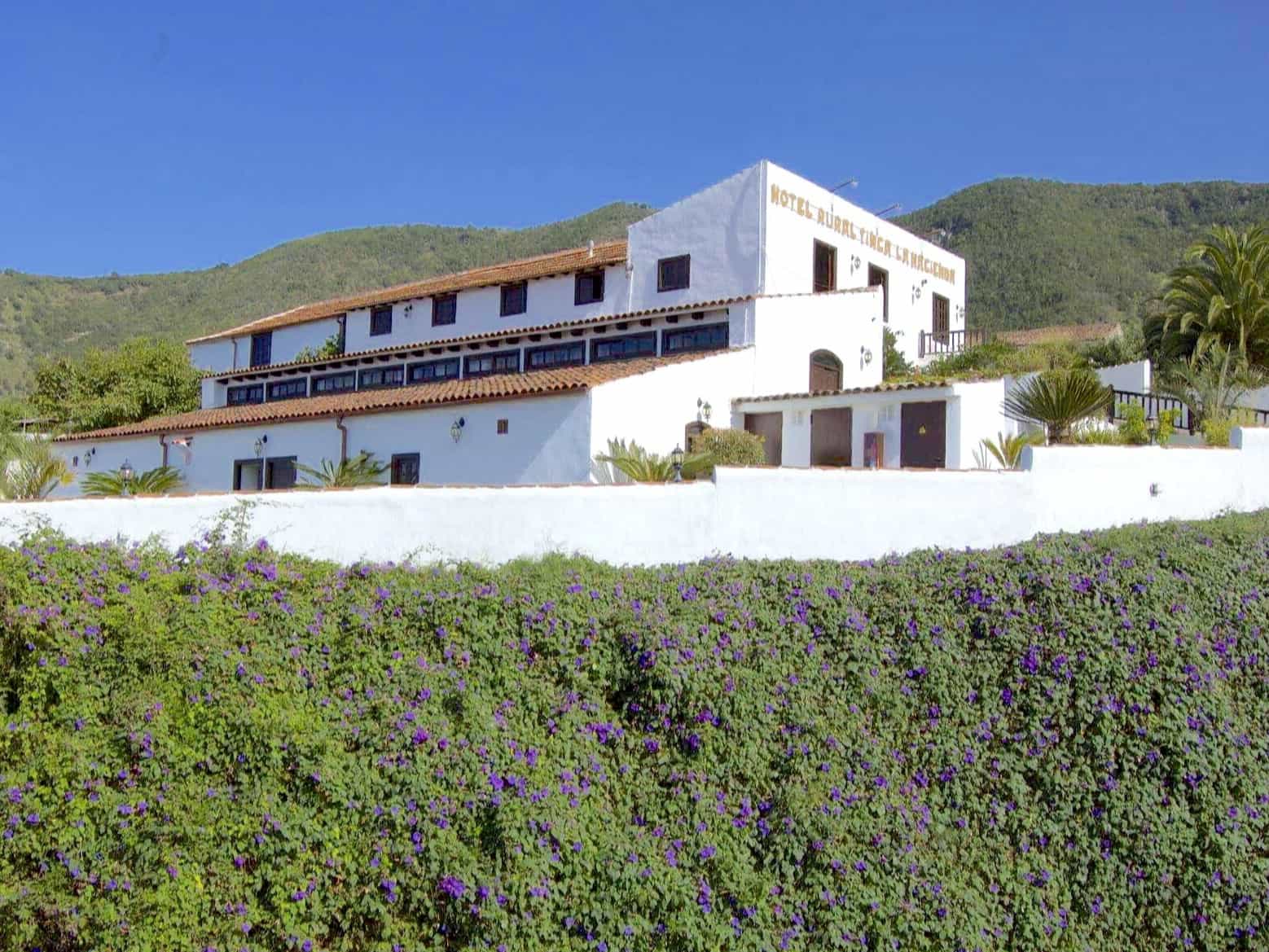 White hotel building of Finca La Hacienda surrounded by plants and vegetation and a blue sky in Tenerife.