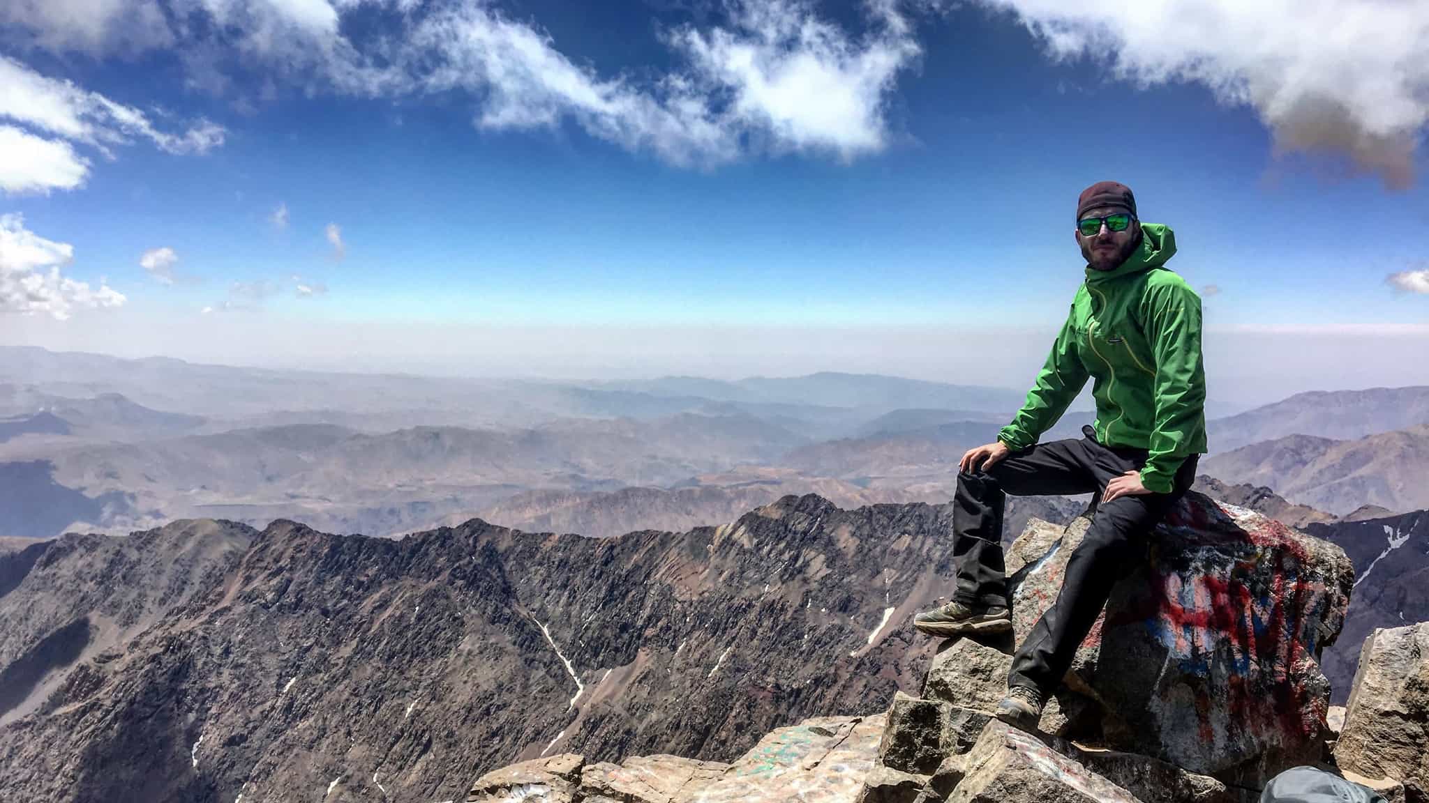 A man sits on a rock at the summit of Mountain Toubkal in the Atlas Mountains, Morocco. 