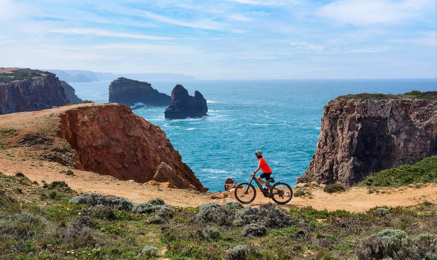 Woman cycling on the the rocky cliffs of the Vicentina coast of Algarve, Portugal