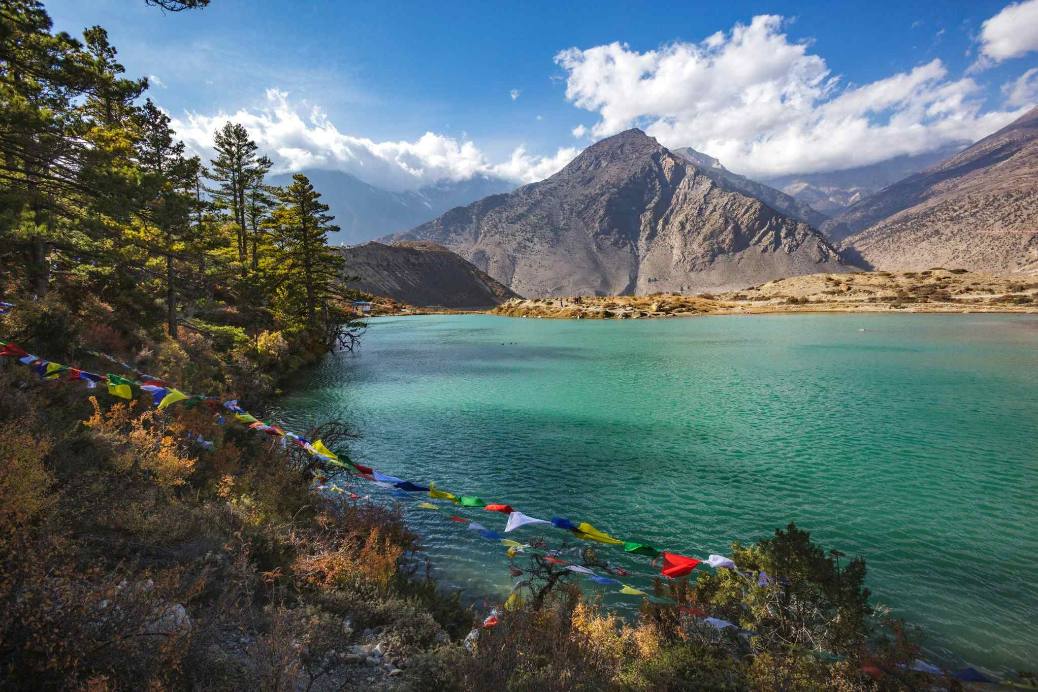 The turquoise waters of Dhumba Lake from Jomson, with prayer flags in the foreground, Nepal