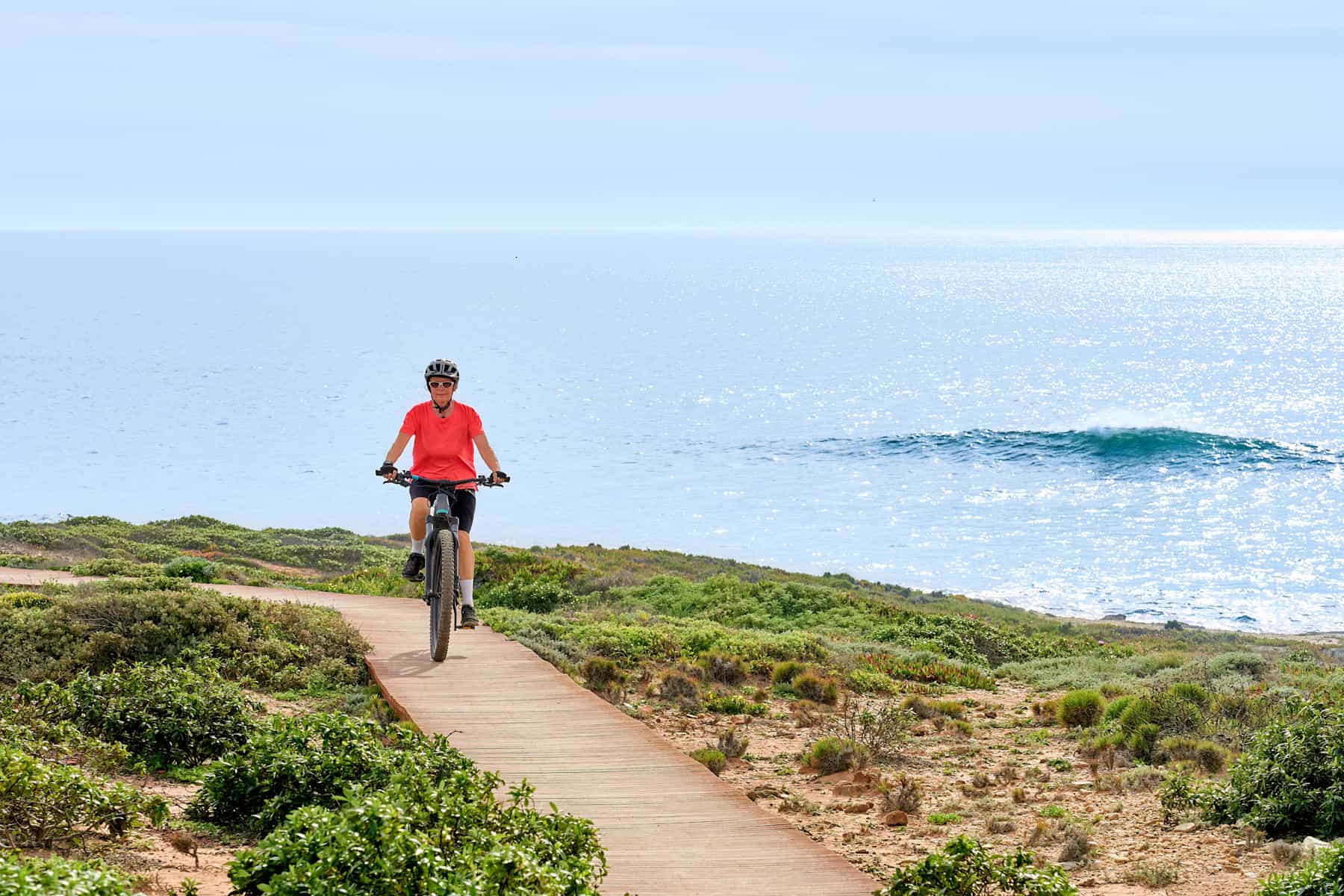 woman riding her electric mountain bike at the rocky and sandy coastline of the atlantic ocean in Porto Covo, Portugal