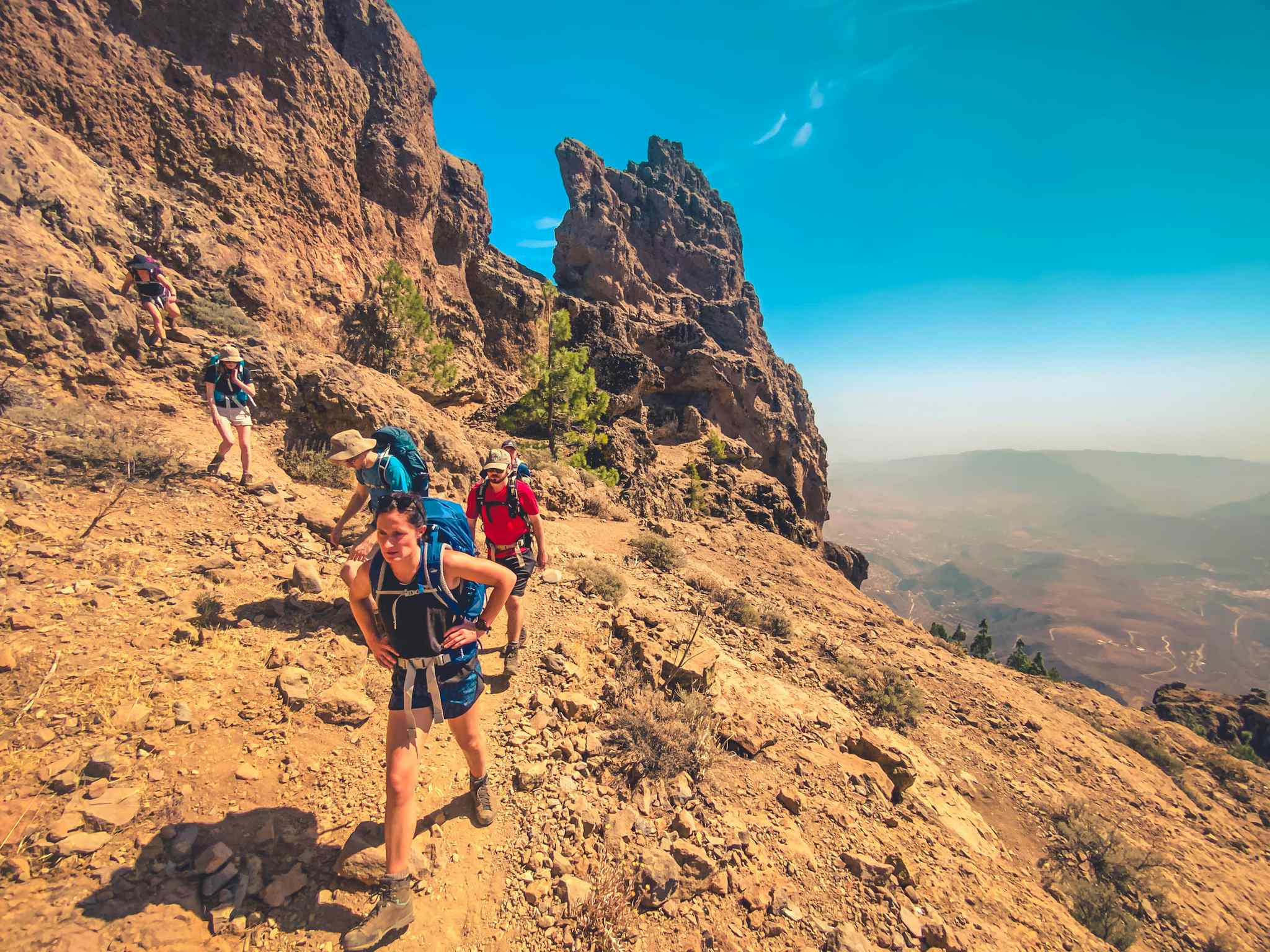 Hikers tackling a dusty trail in Gran Canaria, backed by rocks and blue skies.