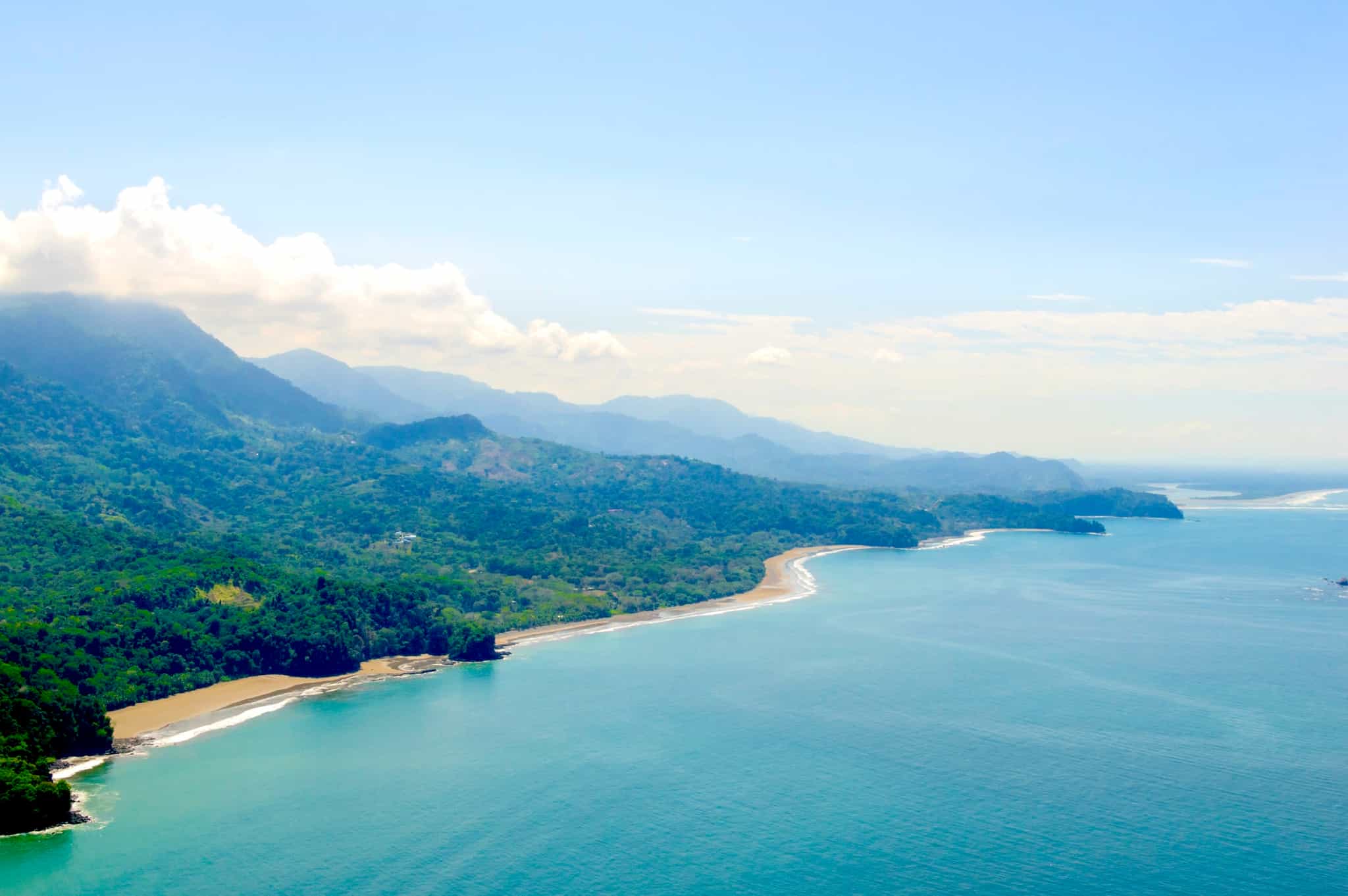 Vibrant tropical forests flow down from the mountains to the sandy beaches along the coast.