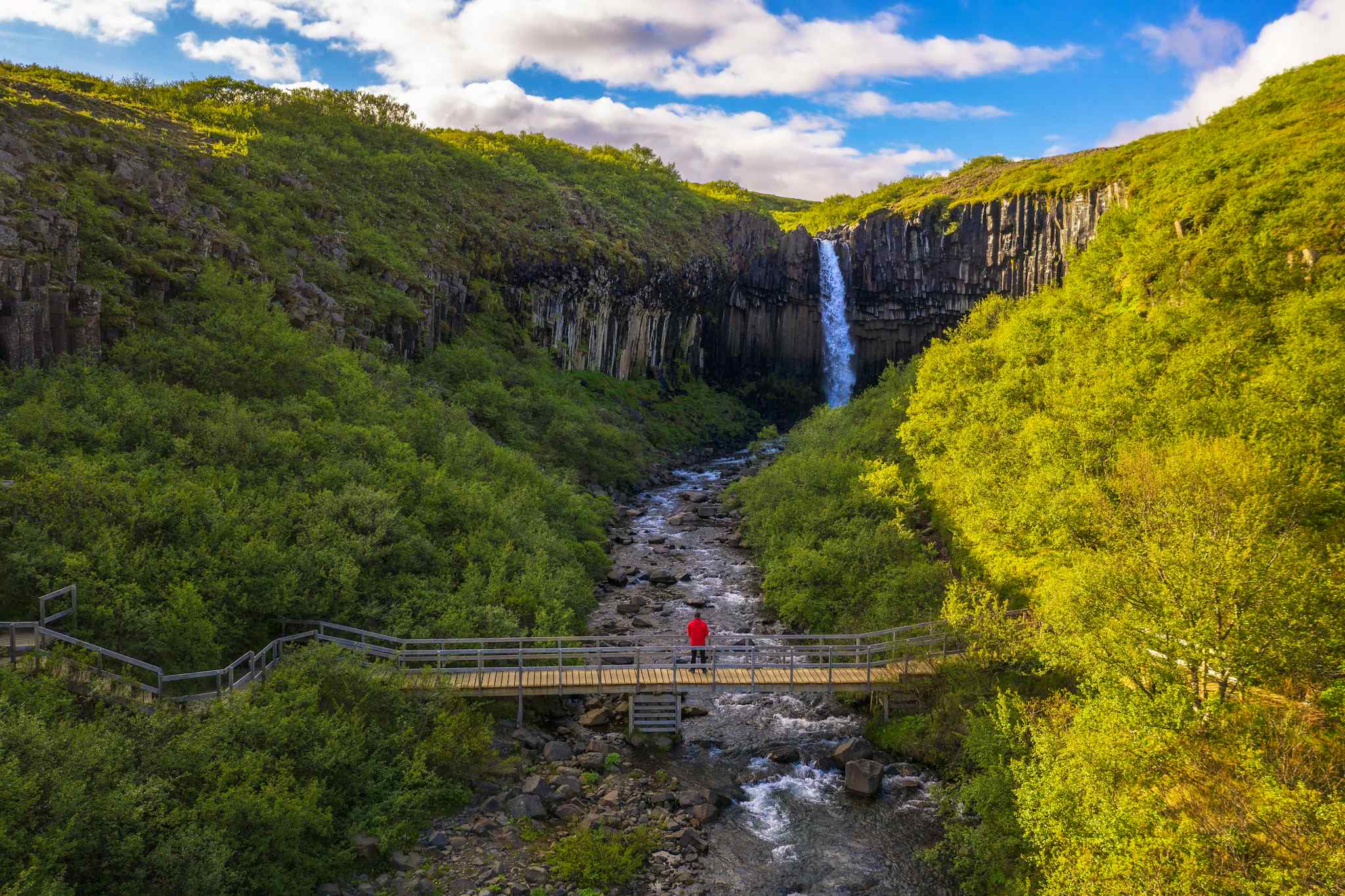 Hiker on a bridge looking at Svartifoss waterfall in Skaftafell National Park, Iceland. Photo: GettyImages-1393966267