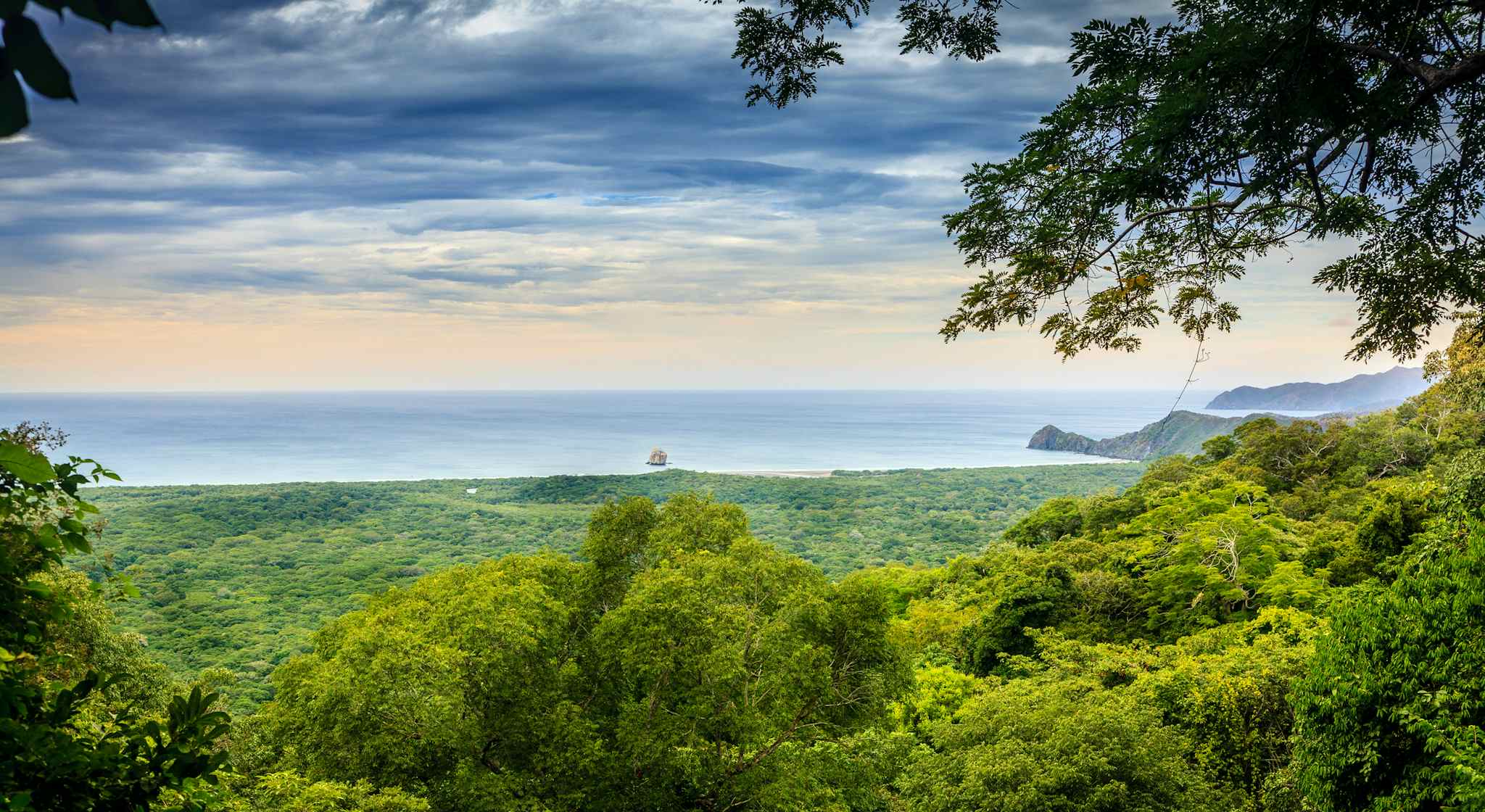 View through a gap in the trees of Costa Rica's Pacific coastline, with forest in the foreground.