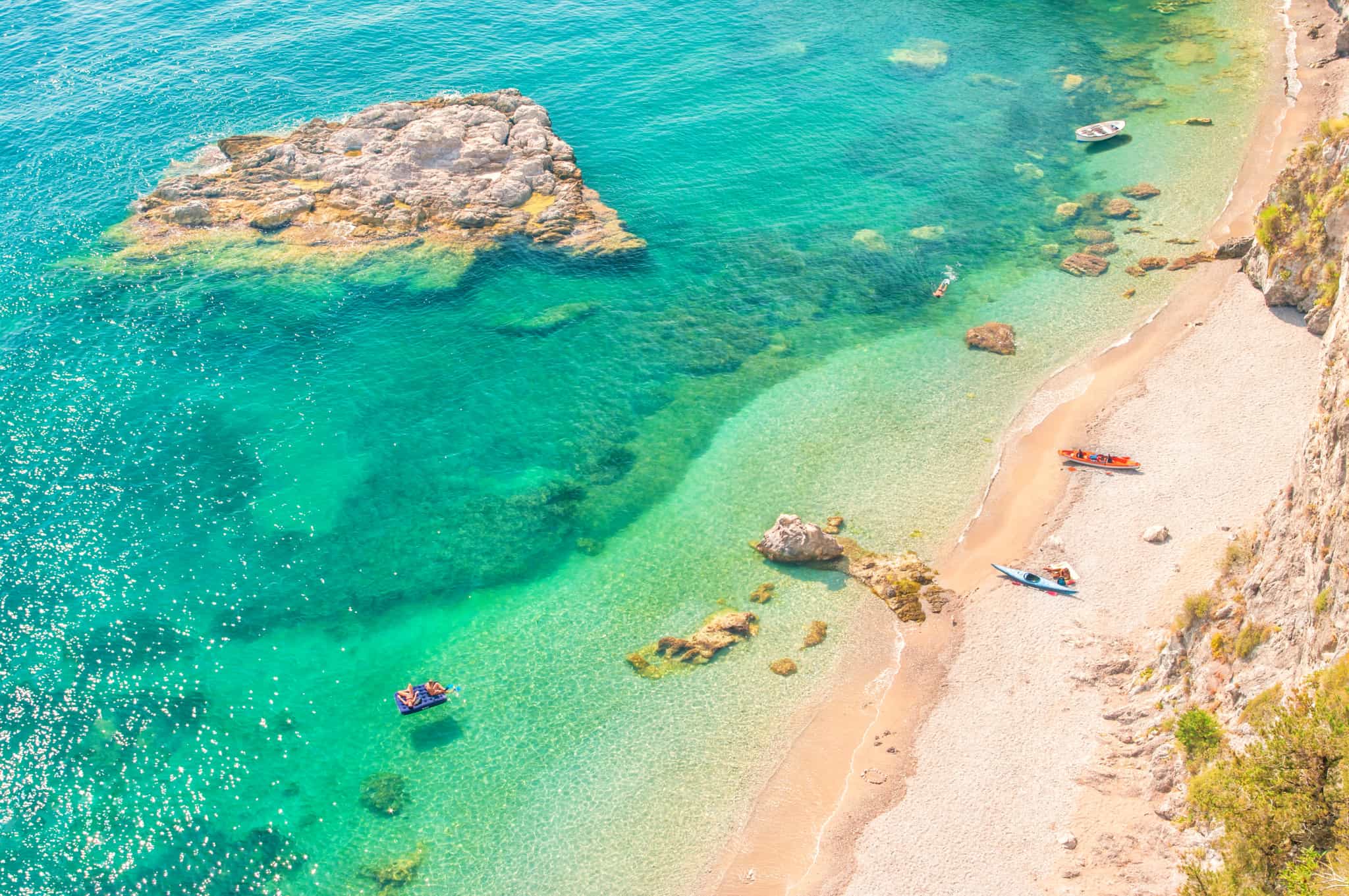 Aerial view of kayaks on an isolated sand beach with turquoise green waters, Greece.