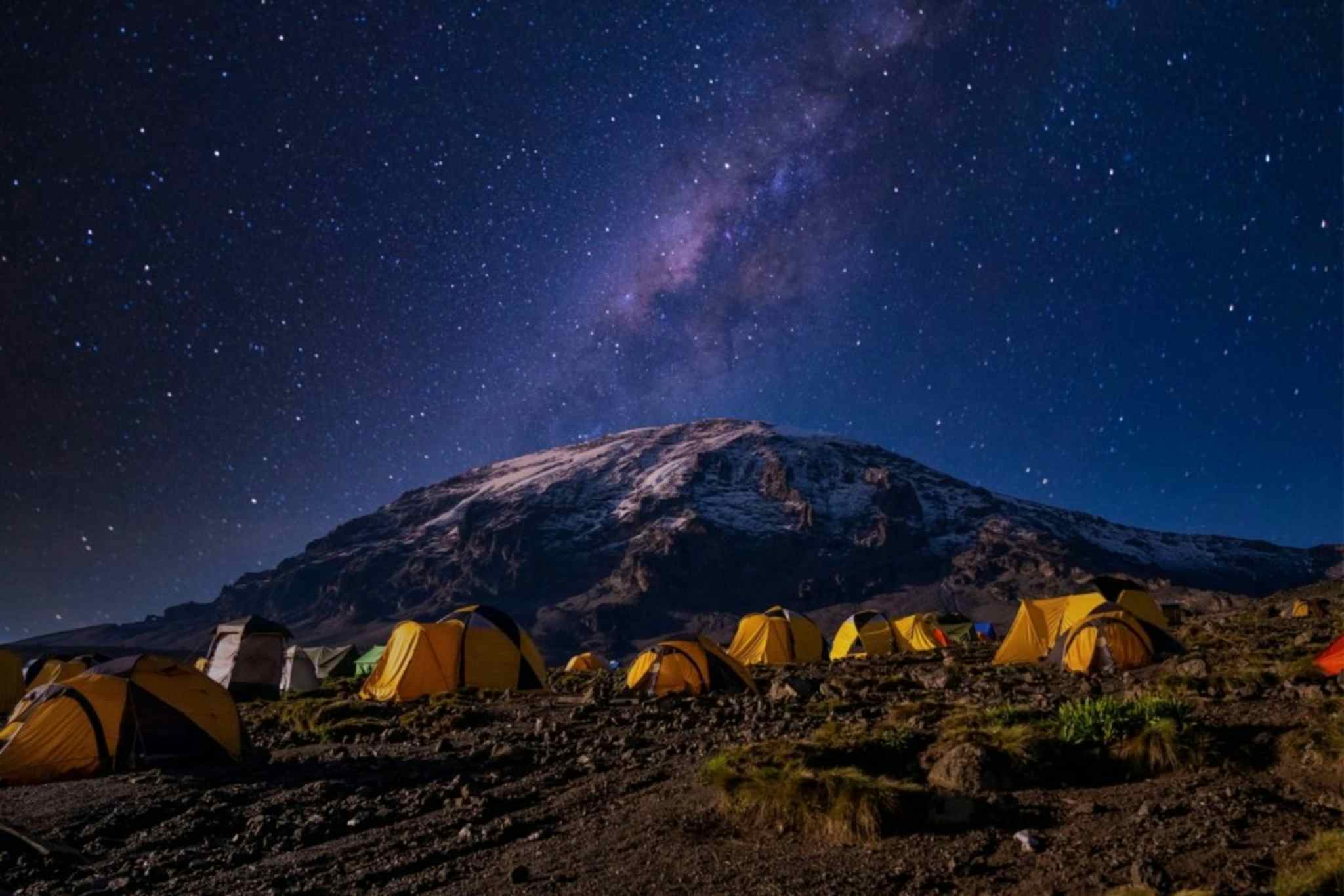 A group of 7 yellow tents in front of the summit of Kilimanjaro, Tanzania under a clear and starry sky.