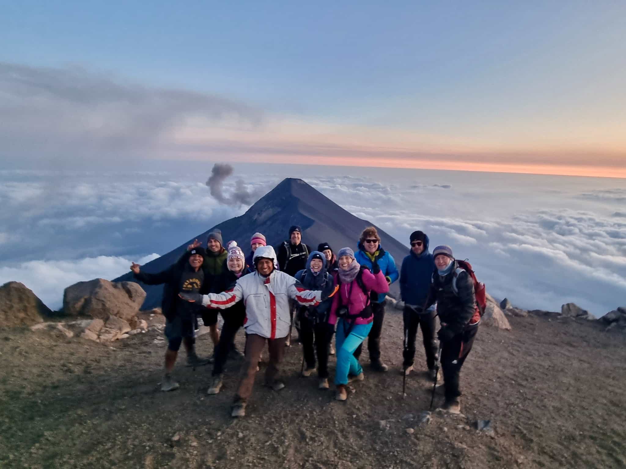 A group poses at the summit of Acatenango volcano with Fuego volcano in the background, Guatemala.