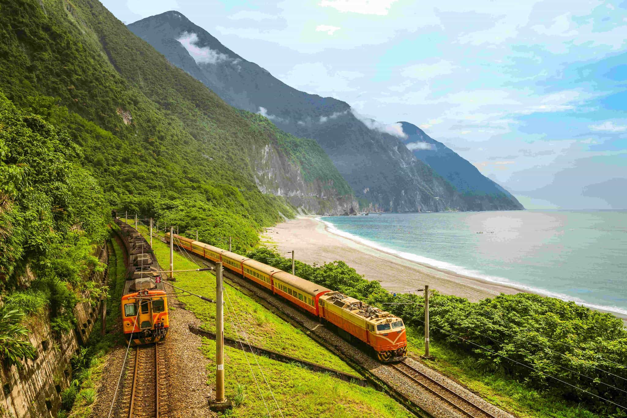 Trains on the Taiwan East Coast Railway, beside a beautiful beach and mountains in the background.
