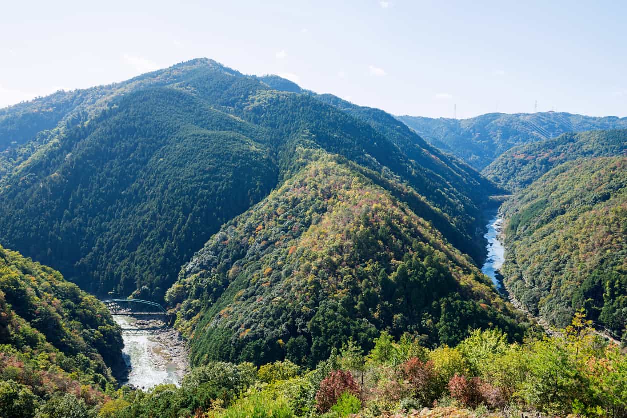 Panoramic view of a river valley and an orange-painted bridge on Mt. Takao in Kyoto Prefecture during the fall season, Japan. Photo: iStock-1285010838