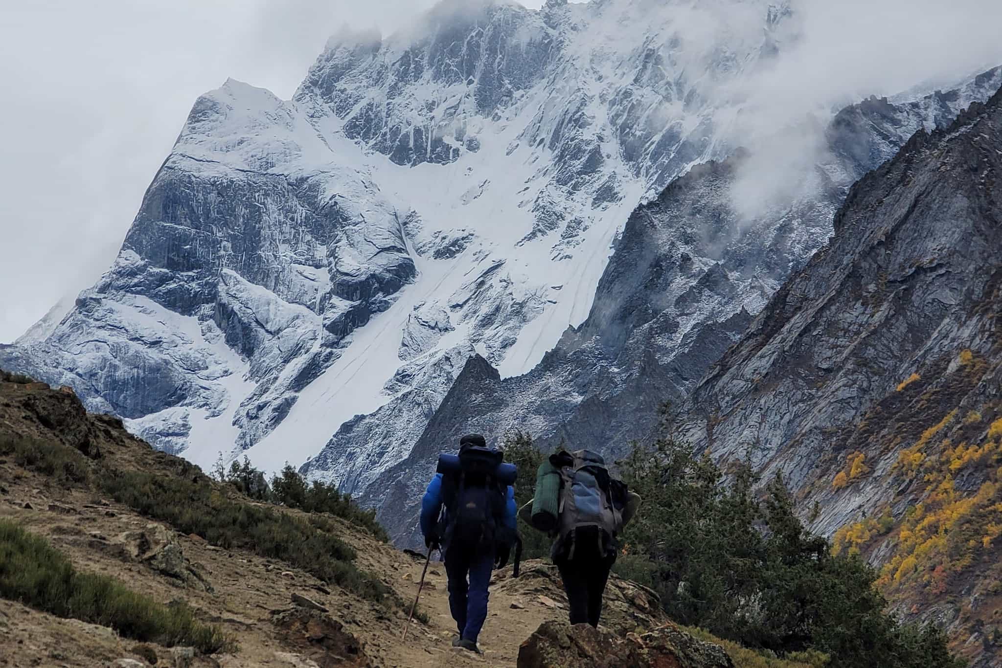 Two hikers climb towards the Charakusa valley below the high snowy mountains