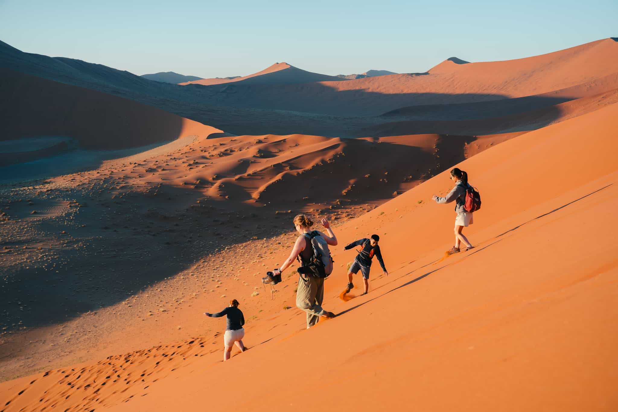 Hikers running down sand dunes in Sossusvlei, Namibia.