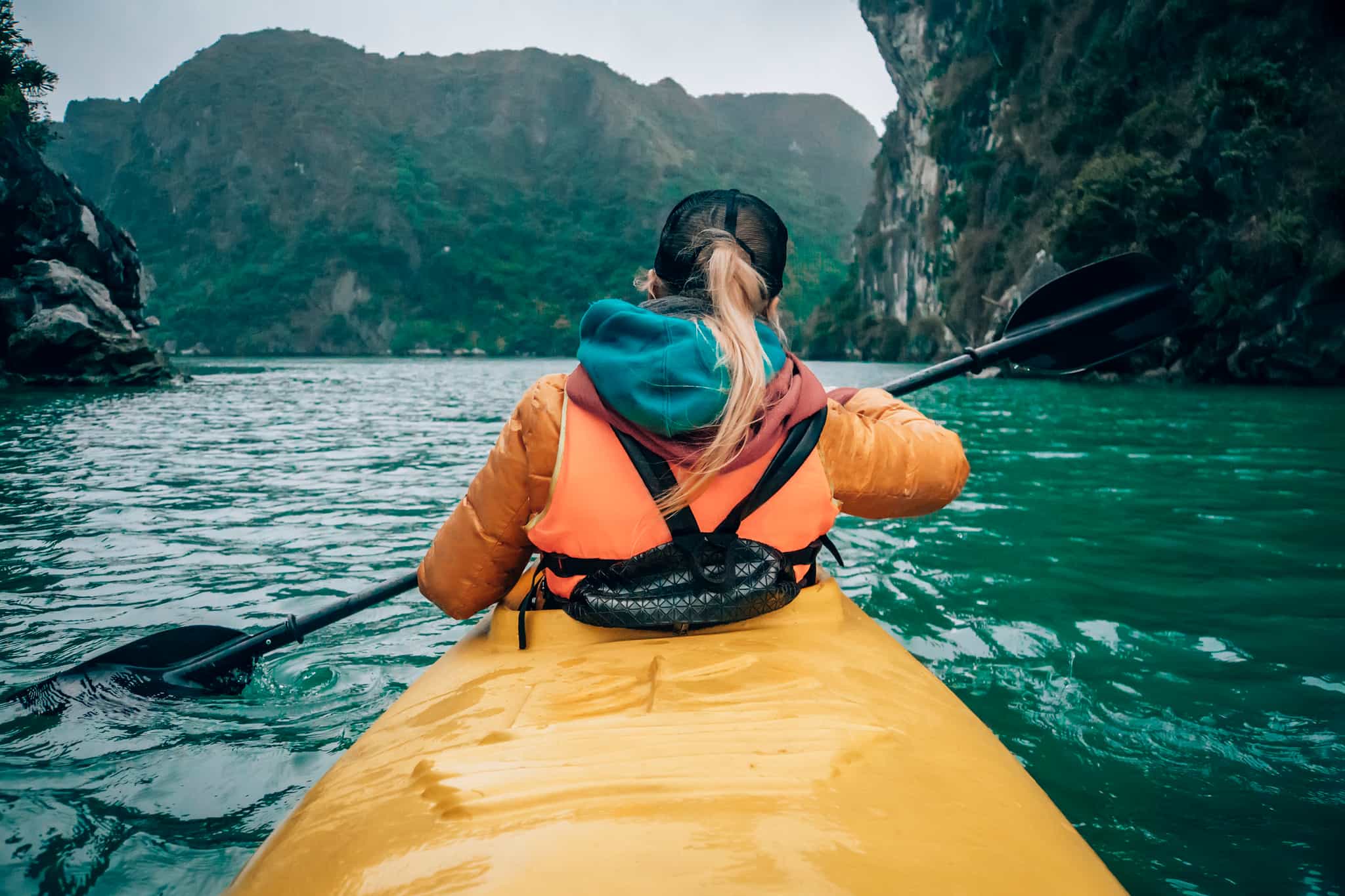 Woman in a yellow kayak paddling through Vietnam's Halong Bay.