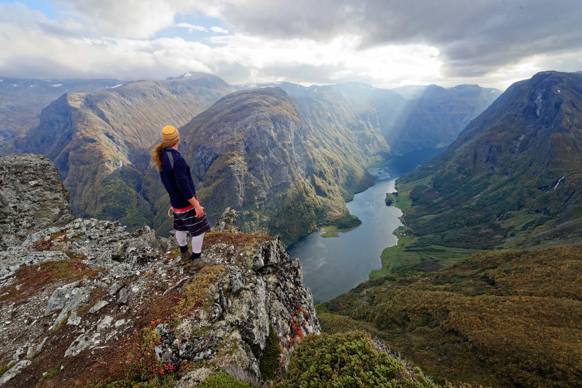 Man standing at the top of Breiskrednosi summit looking over the Nærøyfjord in Norway.