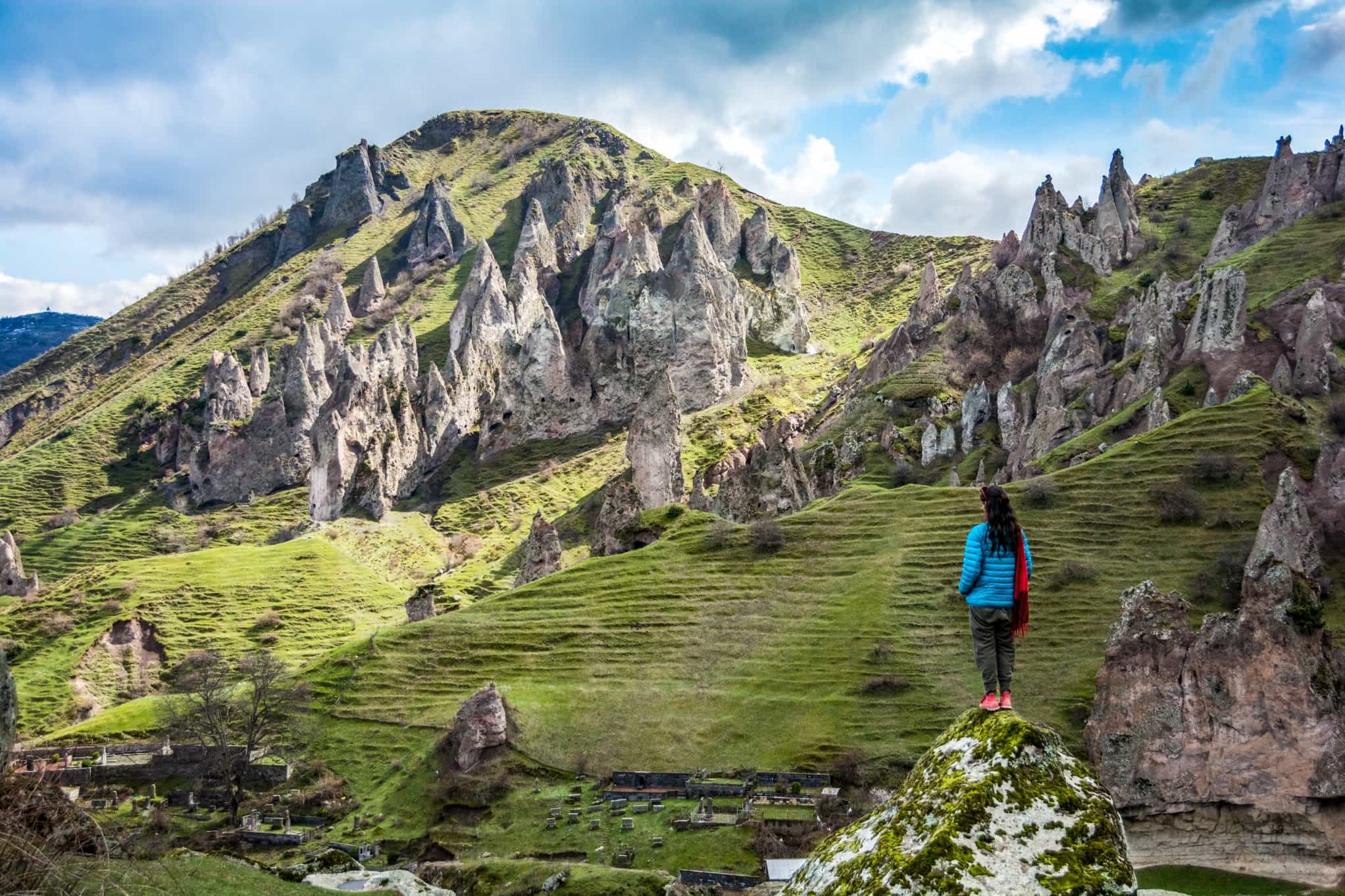 A lone female traveler standing on a rock spire in the shadows while thoughtfully looking out at strange rock formations in the mountains surrounding the city of Goris, Armenia