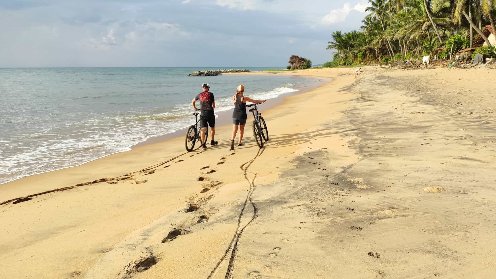 Two cyclists pushing bikes on the beach in Sri Lanka