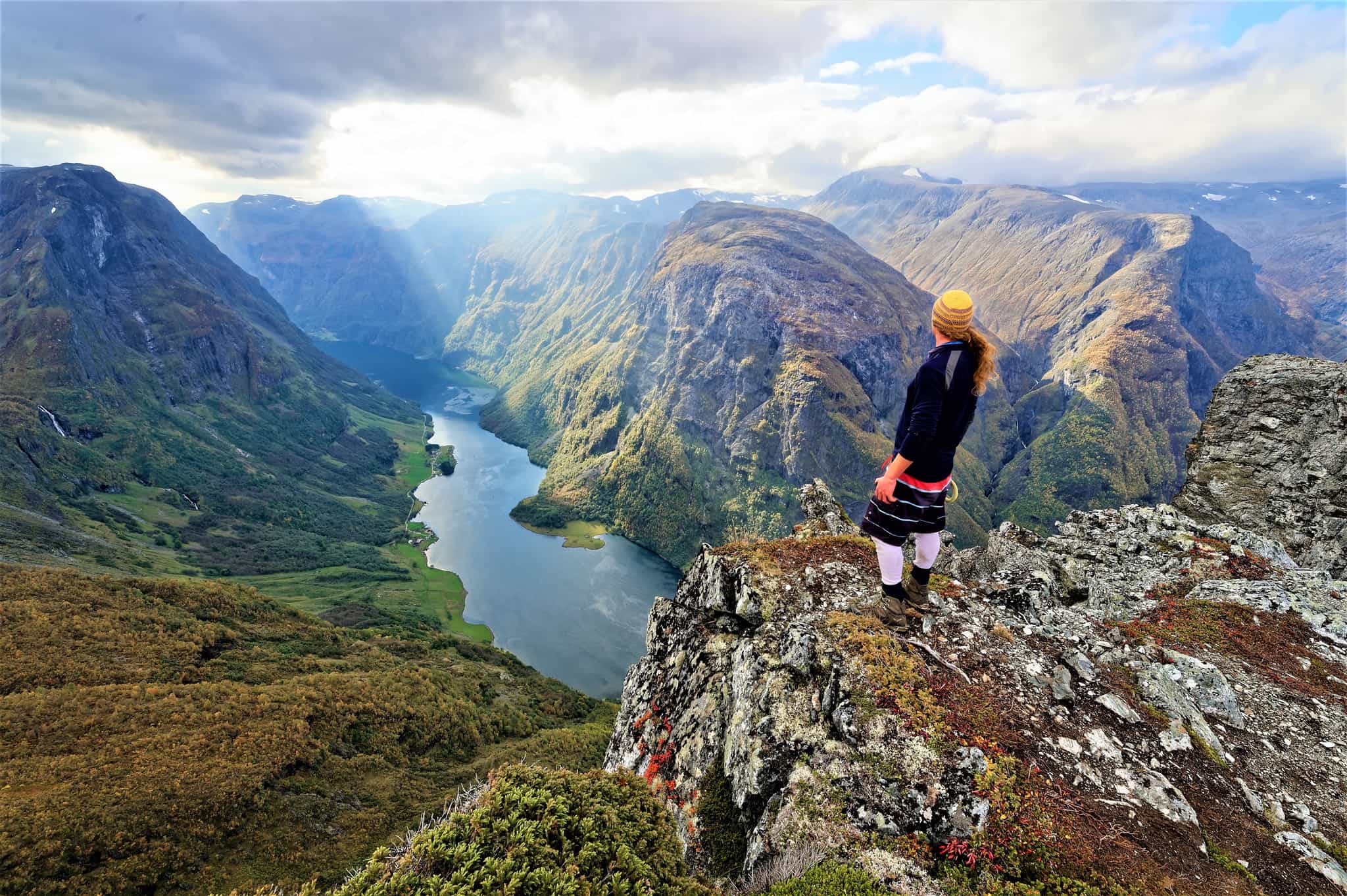 A hiker stands at the edge of the Breiskrednosi summit looking over the Naeroyfjord in the Norwegian Fjords.