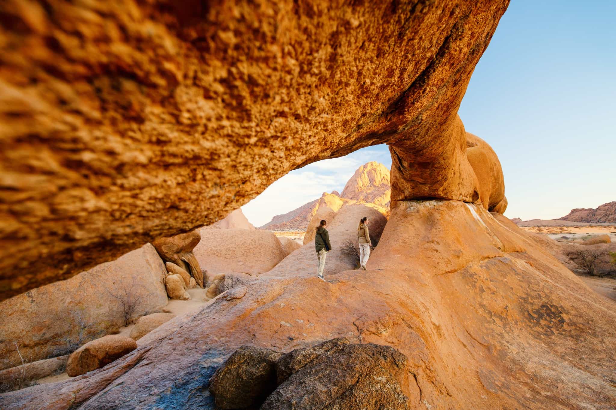 Two people hiking below the Spitzkoppe Arch in Namibia