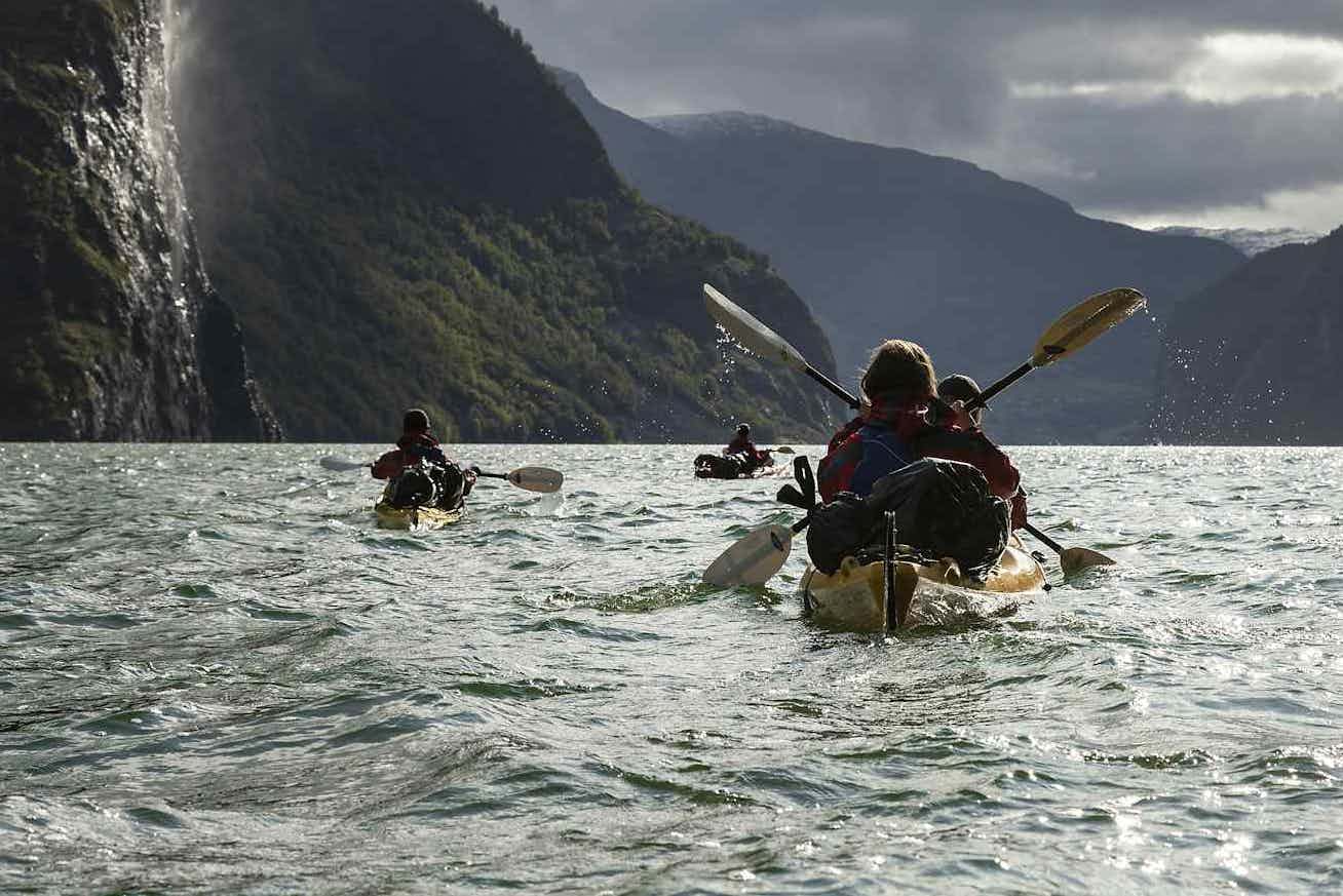 A group of kayakers paddle along the Naeroyfjord next to a waterfall in the Norwegian Fjords.