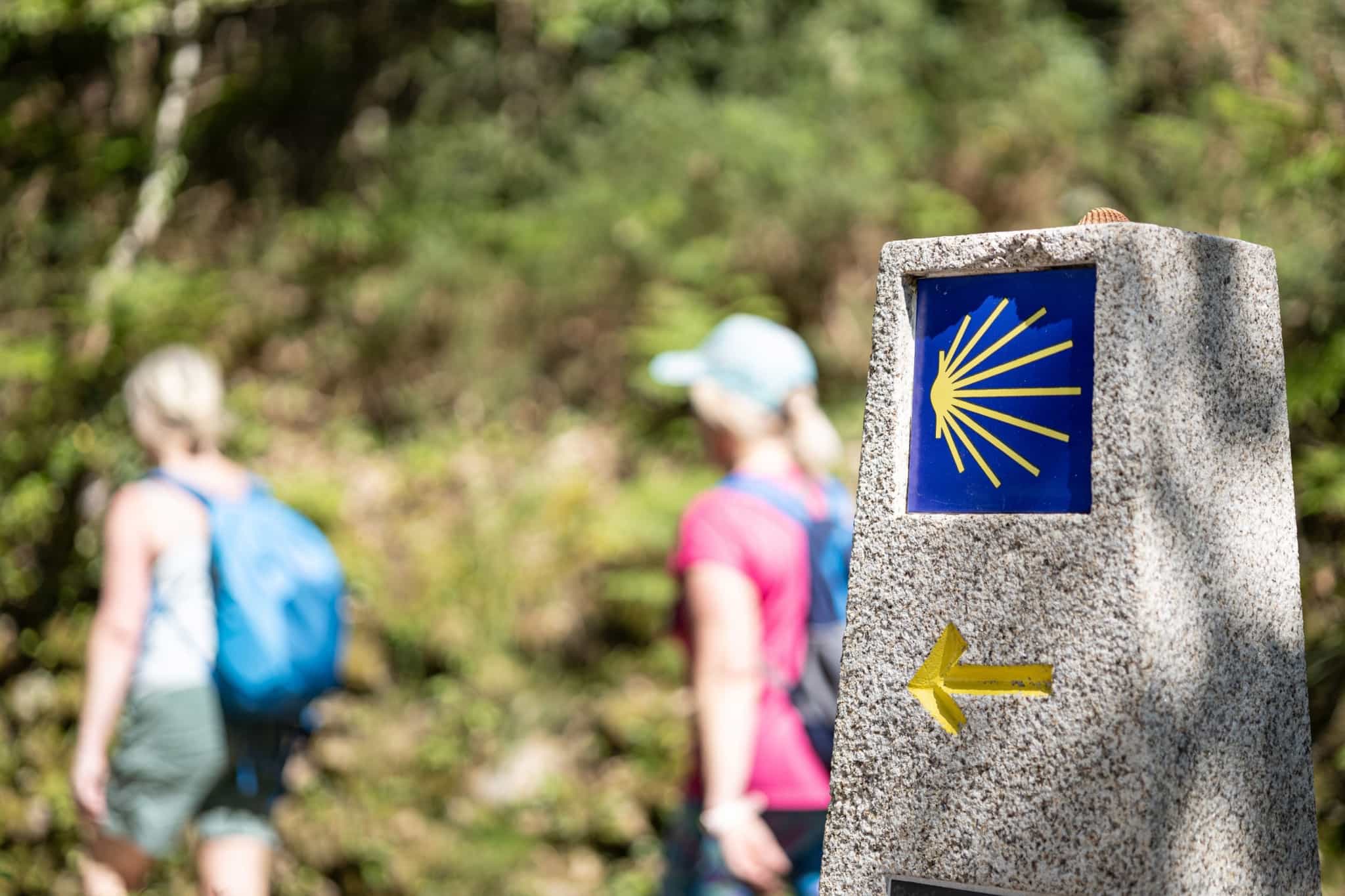 Hikers walking past the iconic waymarker sign of the Camino de Santiago, Galicia, Spain.
