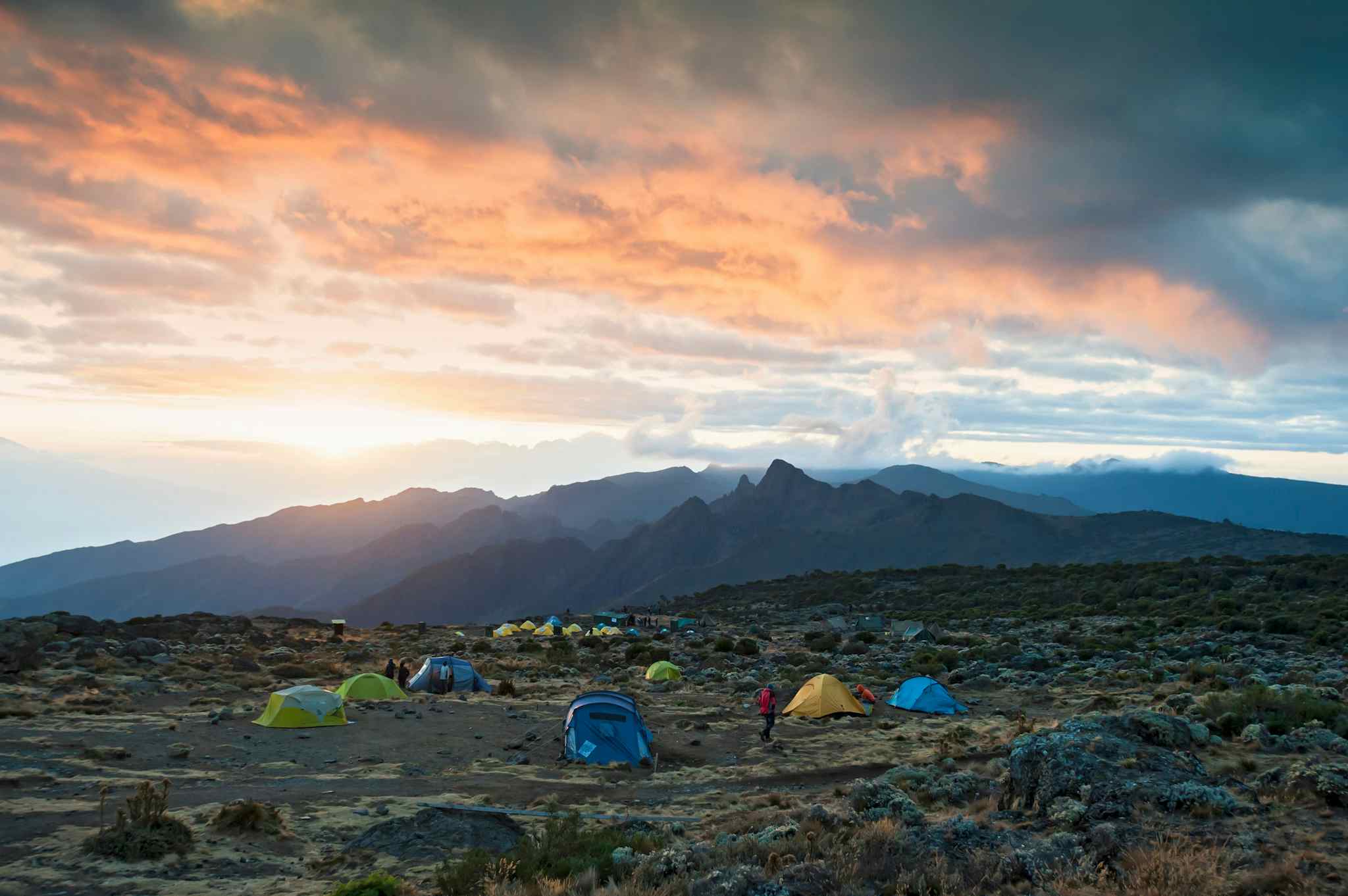 Colourful tents at Shira Camp on Mount Kilimanjaro, with mountains and sunset coloured clouds in the background.