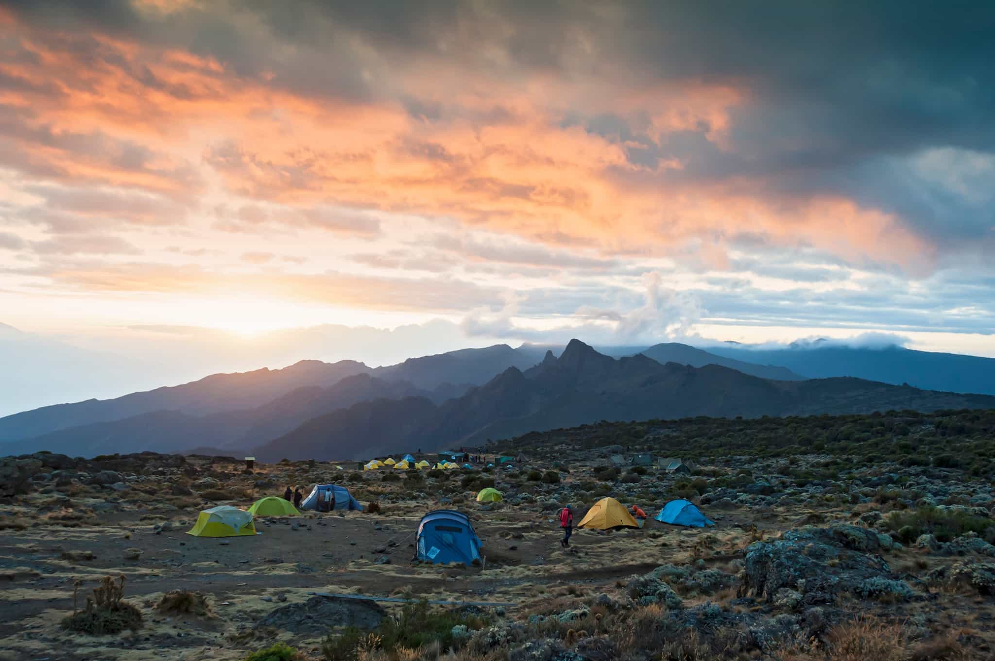 Colourful tents at Shira Camp on Mount Kilimanjaro, with mountains and sunset coloured clouds in the background.