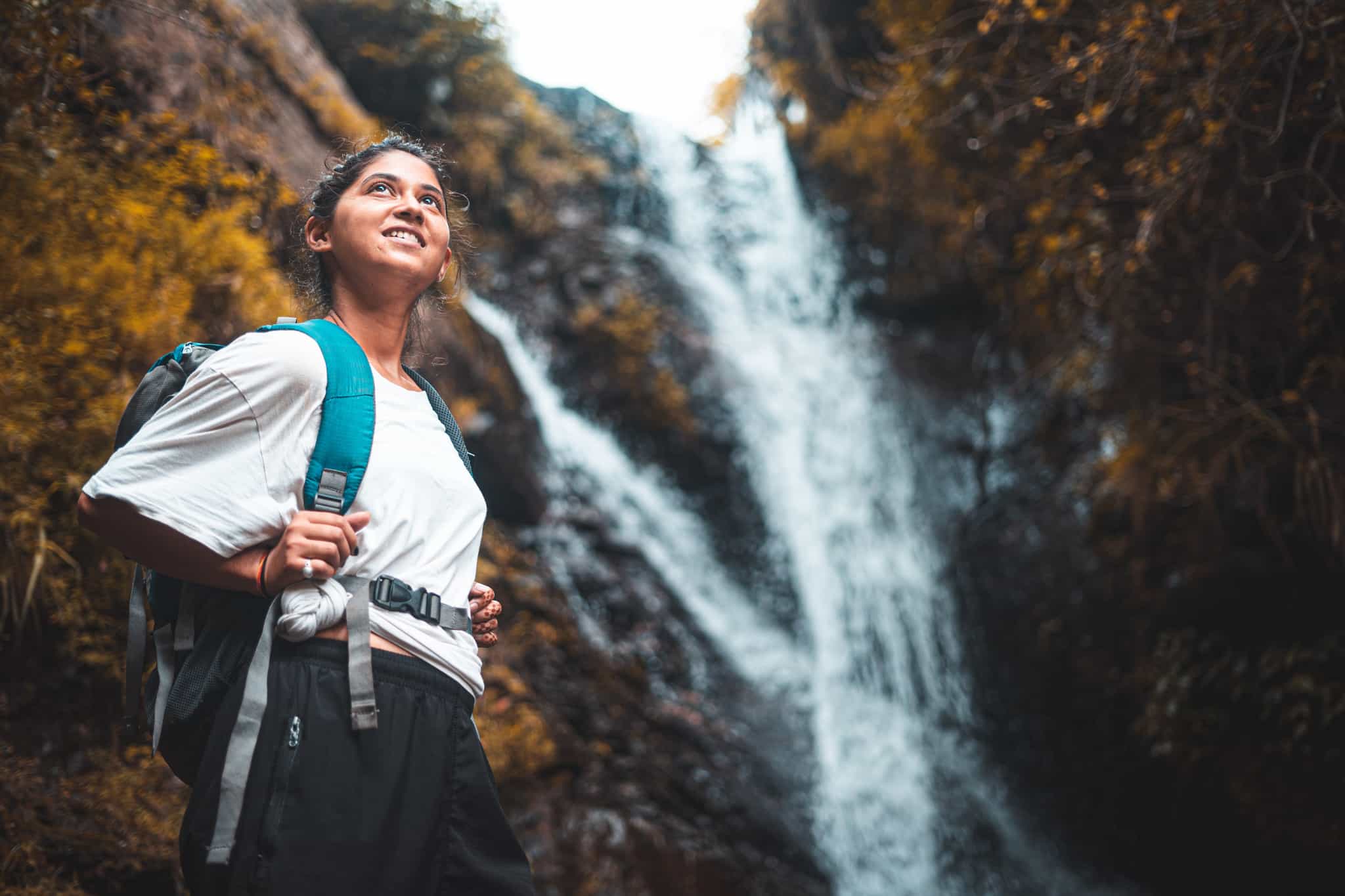 Hiker carrying a backpack standing in front of a waterfall in the forest