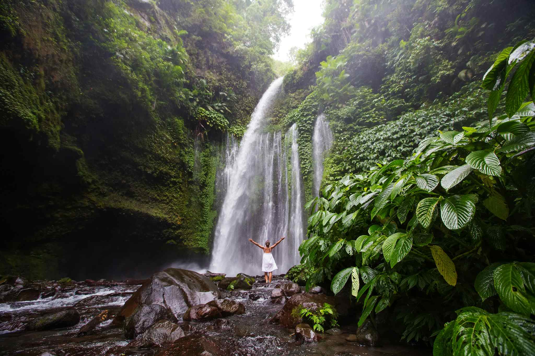 Woman standing in front of Senaru Waterfall on Lombok island, Indonesia. Photo: GettyImages-977697236