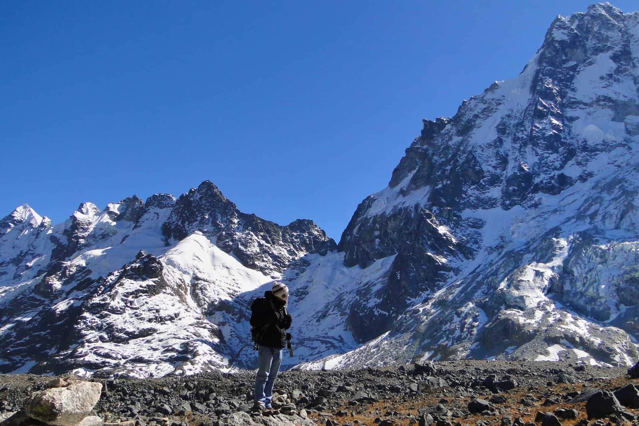 Hiker stands at the top of Salkantay Pass with snowy mountains in the background