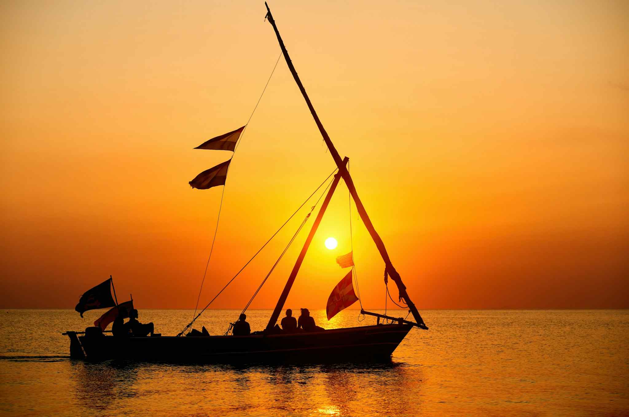 Silhouette of a boat on the ocean with orange sunset behind, Zanzibar.