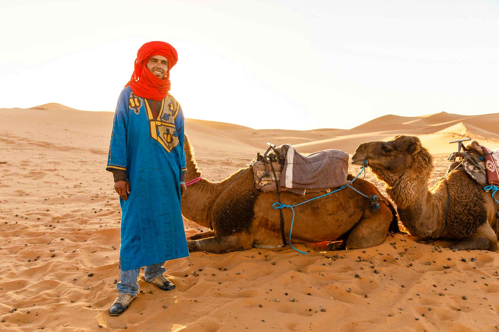 A Berber guide stands beside a camel in the Sahara Desert, Morocco. 