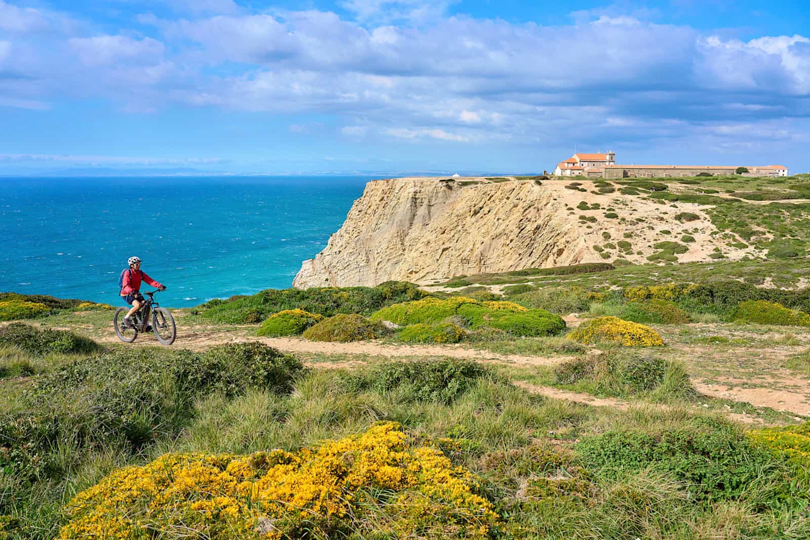 Woman cycling with her electric mountain bike on the cliffs of Cabo Espichel, Portugal