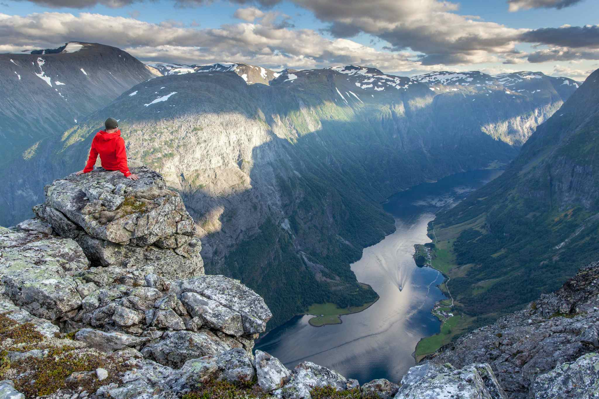 A man sits on a cliff edge in the highlands of above the Naeroyfjord in the Norwegian Fjords.