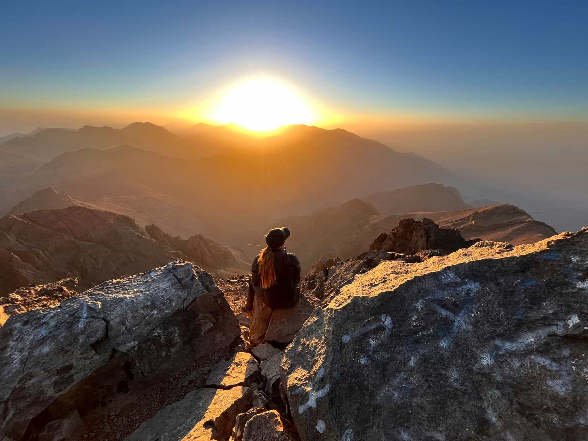 Woman sat looking at the sunrise on Toubkal's summit in Morocco.