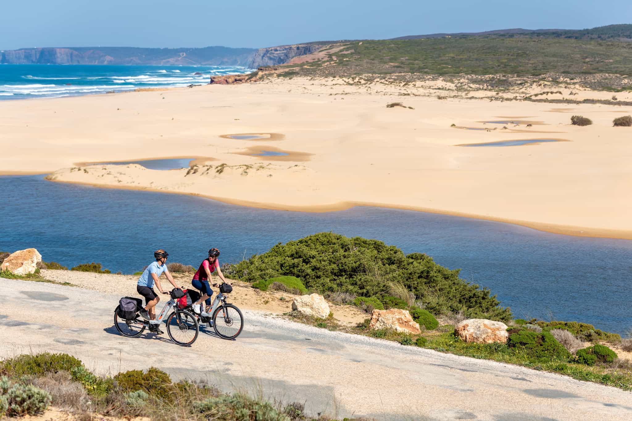 Two cyclists pedalling by Odeceixe beach in Portugal
