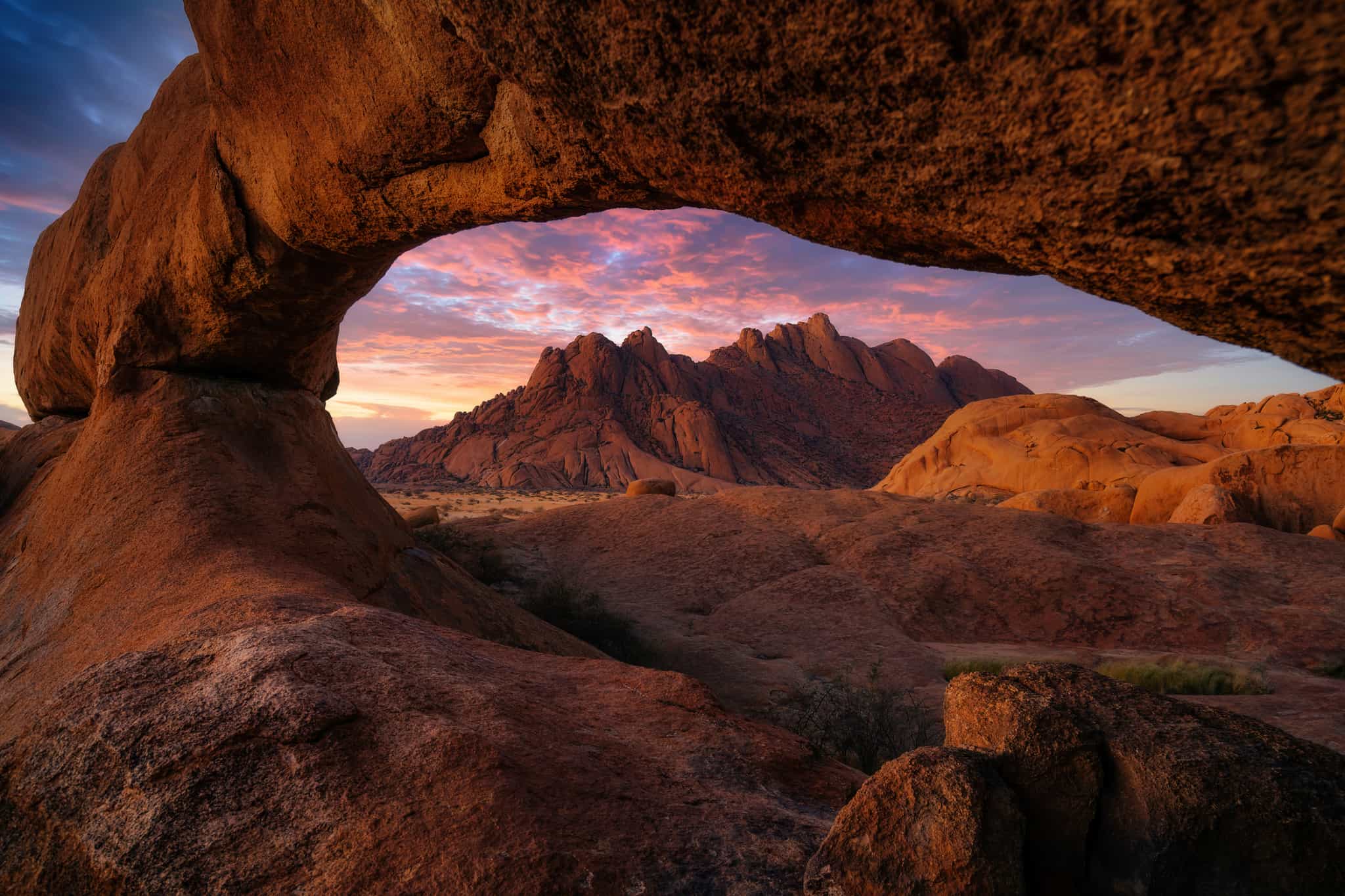 Looking through a natural rock arch at a dramatic sunset over Spitzkoppe, Namibia.
