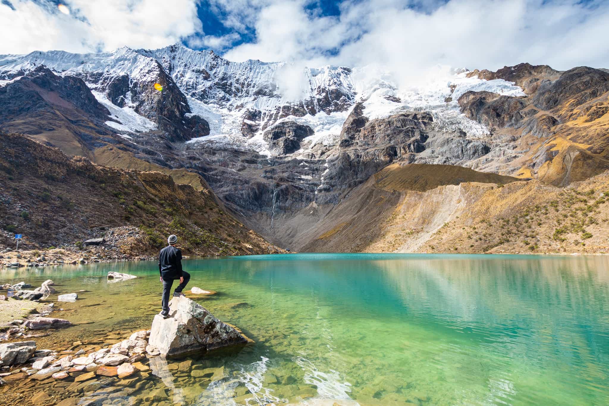 Hiker stands on a rock beside Humantay Lake