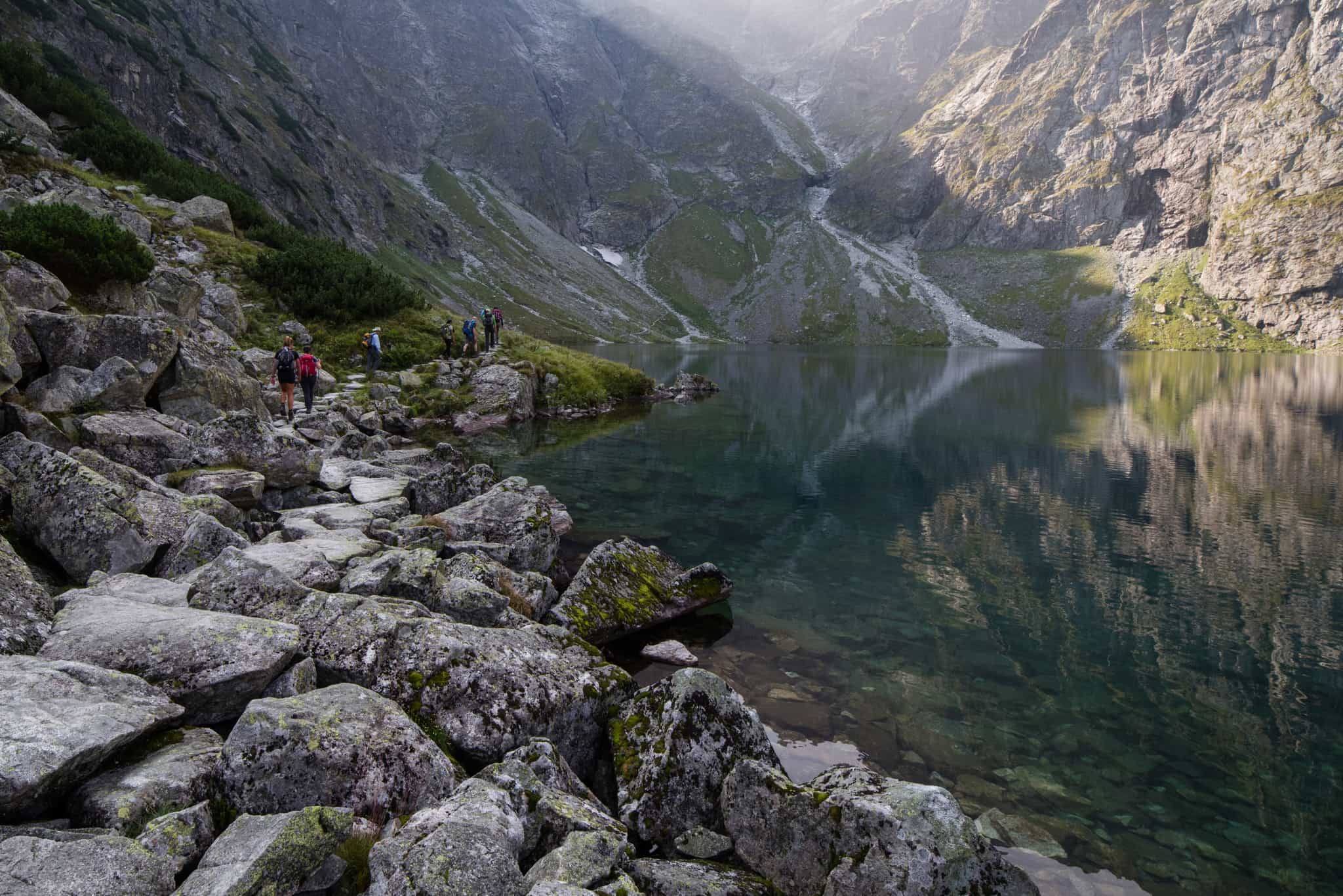 Hikers walking along the shoer of a mountain lake in the Tatras