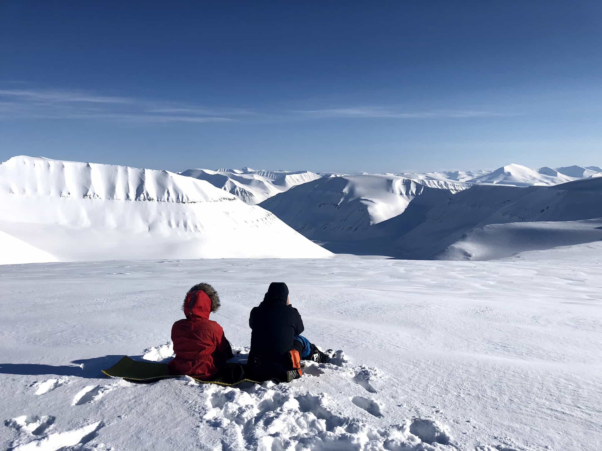 Two people sitting in the snow looking over the pristine winter landscapes of Svalbard.