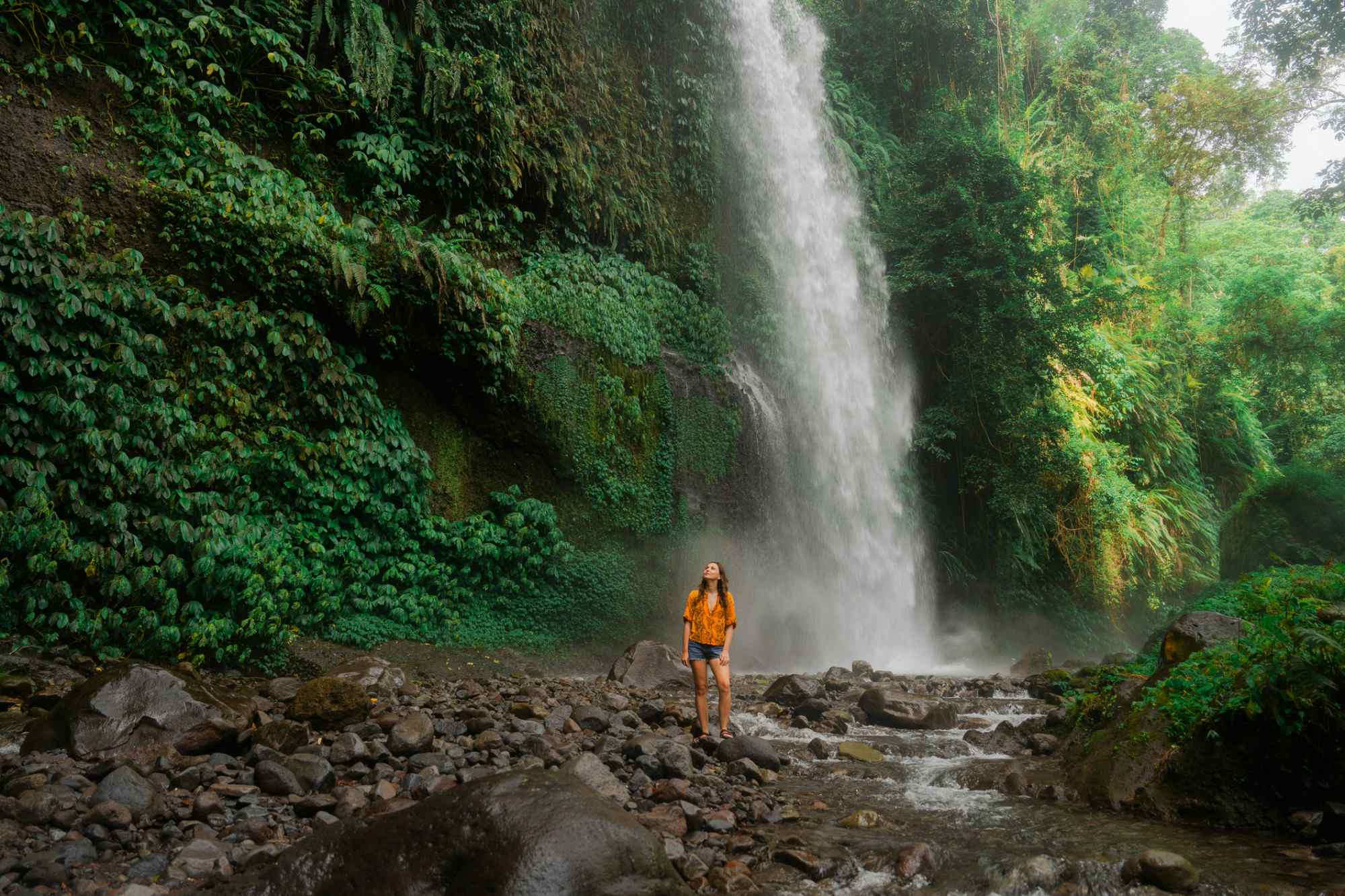 Woman hiker passing by a waterfall in Bali, Indonesia. 